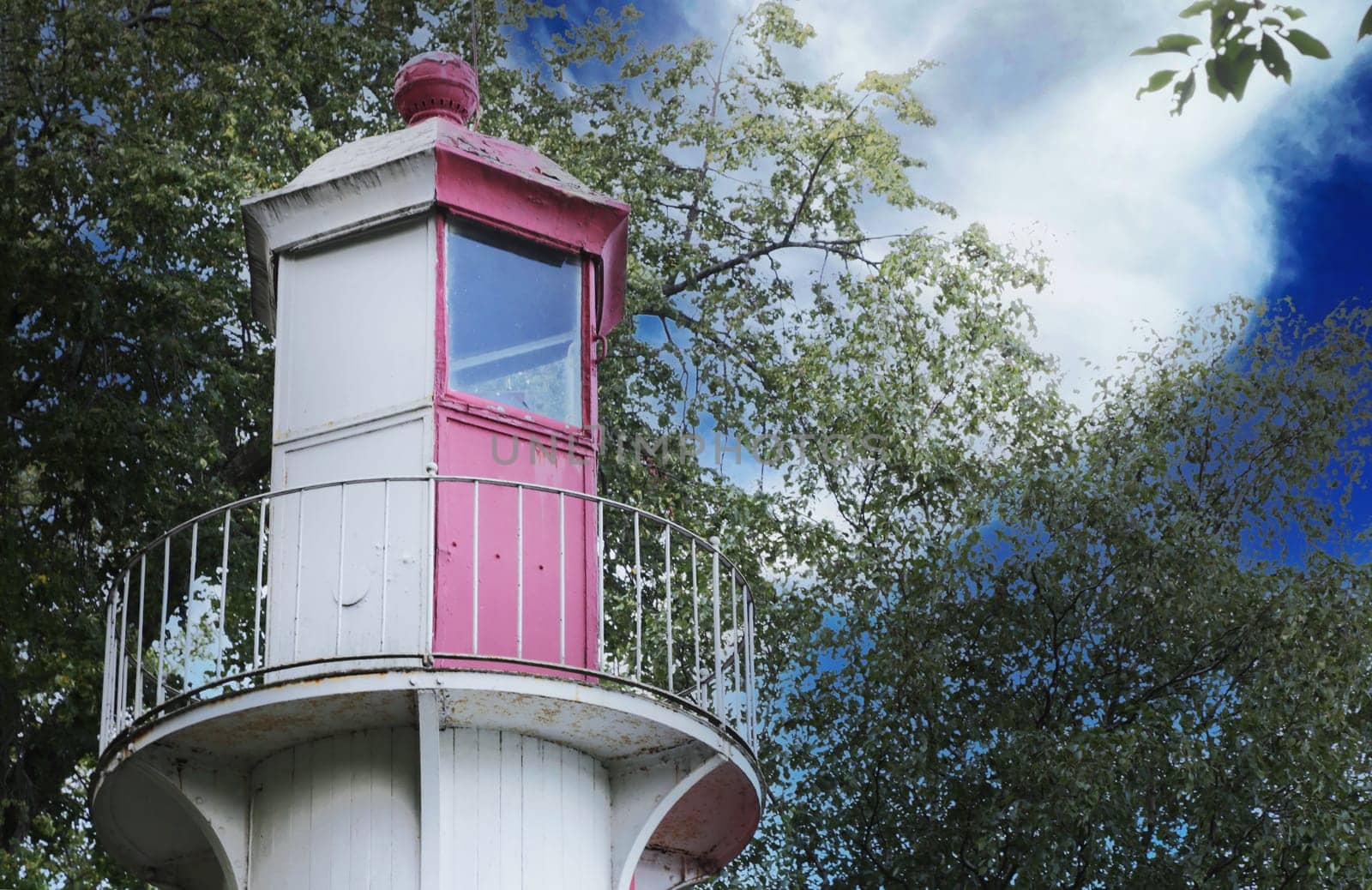 Top of lighthouse, door, window, fence against sky and forest.