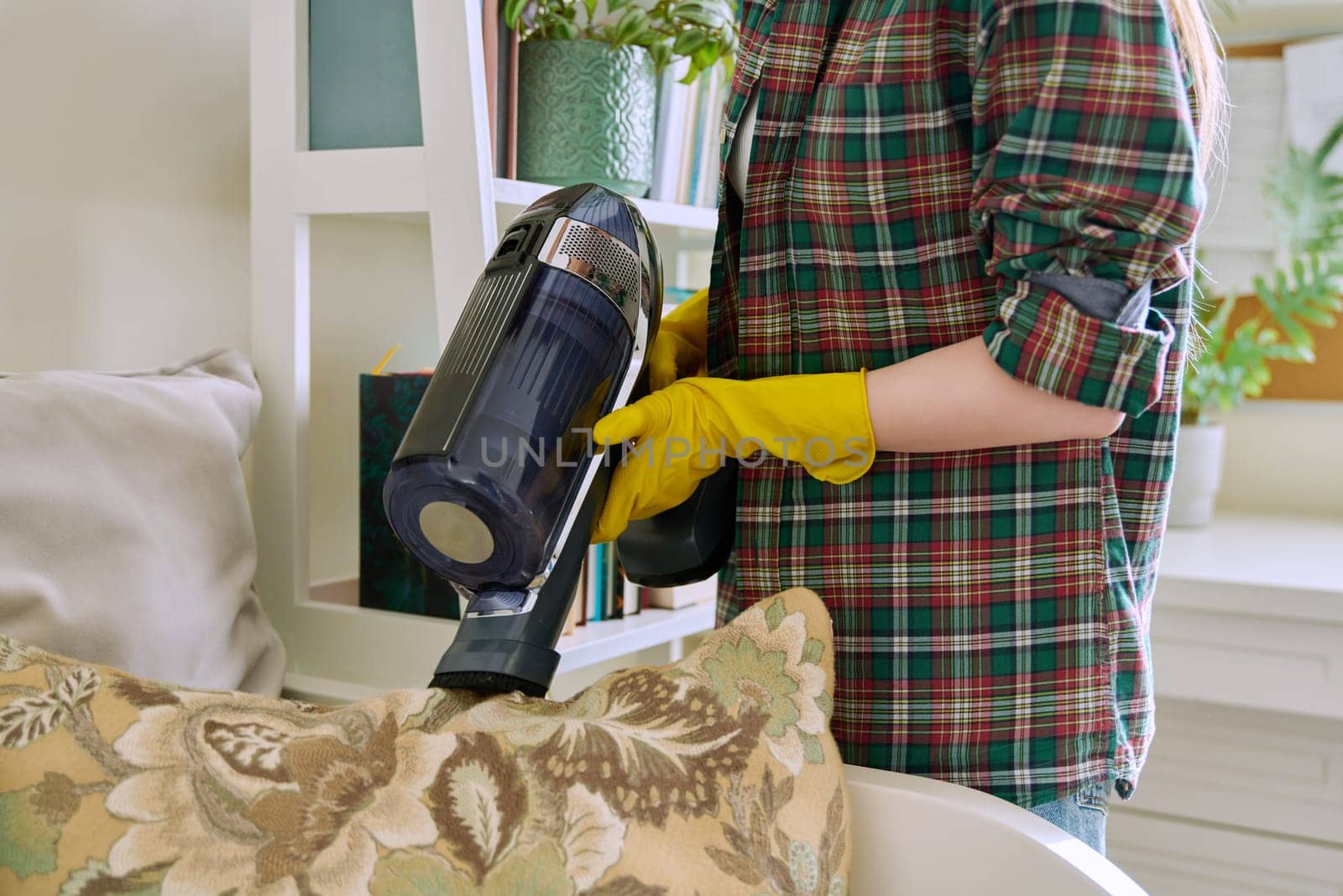 Young woman doing vacuuming, vacuuming pillows on couch. Cleanliness, cleaning, hygiene, youth concept