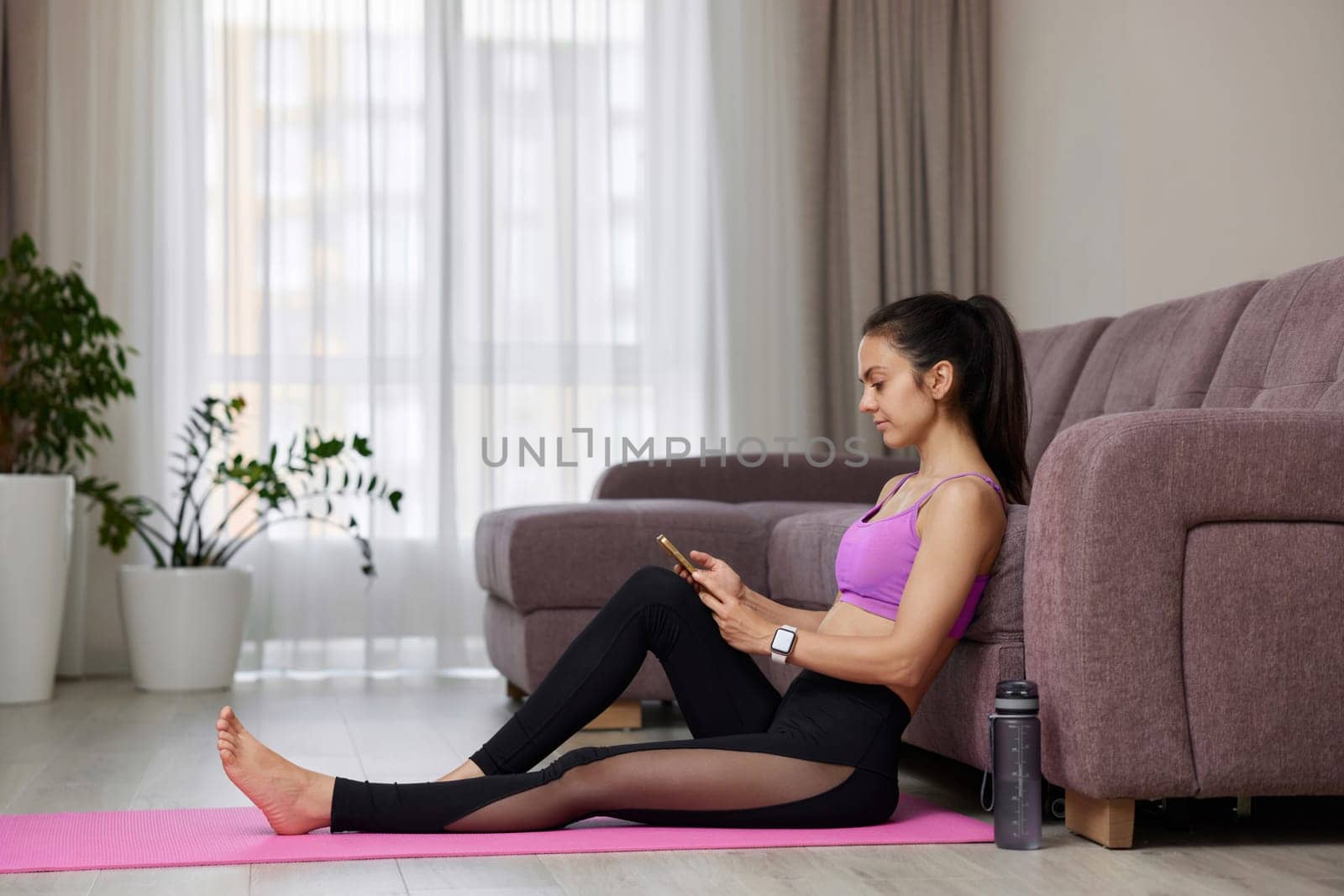 Caucasian sporty woman using smartphone and taking break after yoga practice at home