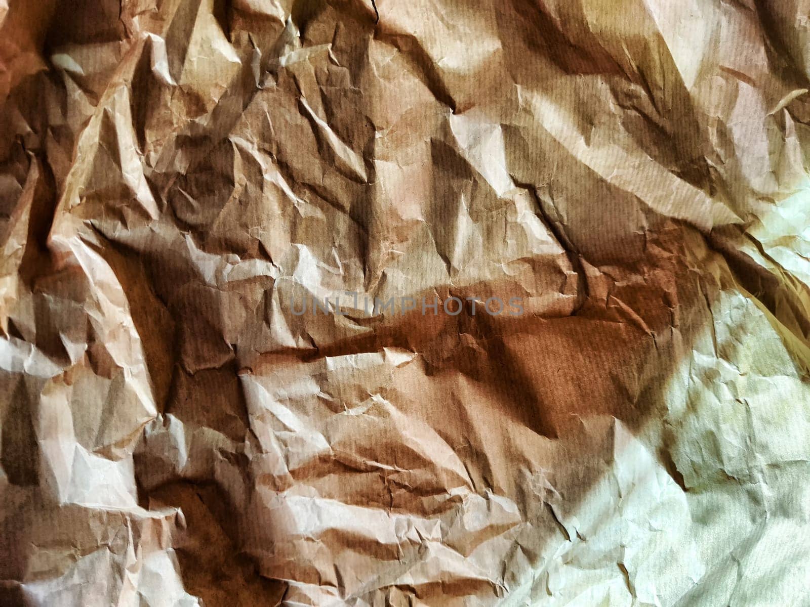Heavily crumpled textured kraft paper in sunlight and with shadow. Abstract background, texture, frame, place for text and copy space