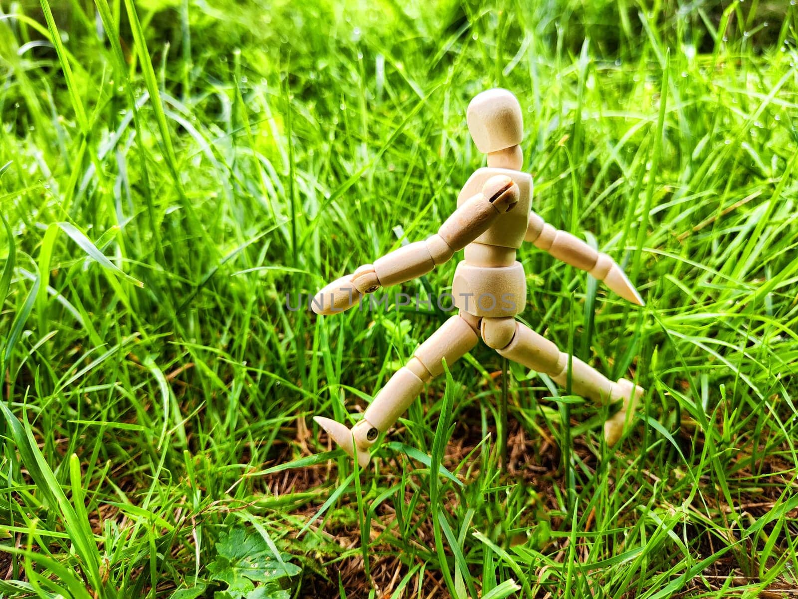 Wooden toy mannequin in forest among grass and trees in summer, autumn, spring. The concept of outdoor recreation and hiking. Healthy lifestyle. Earth Day. Save planet concept. Partial focus, blur