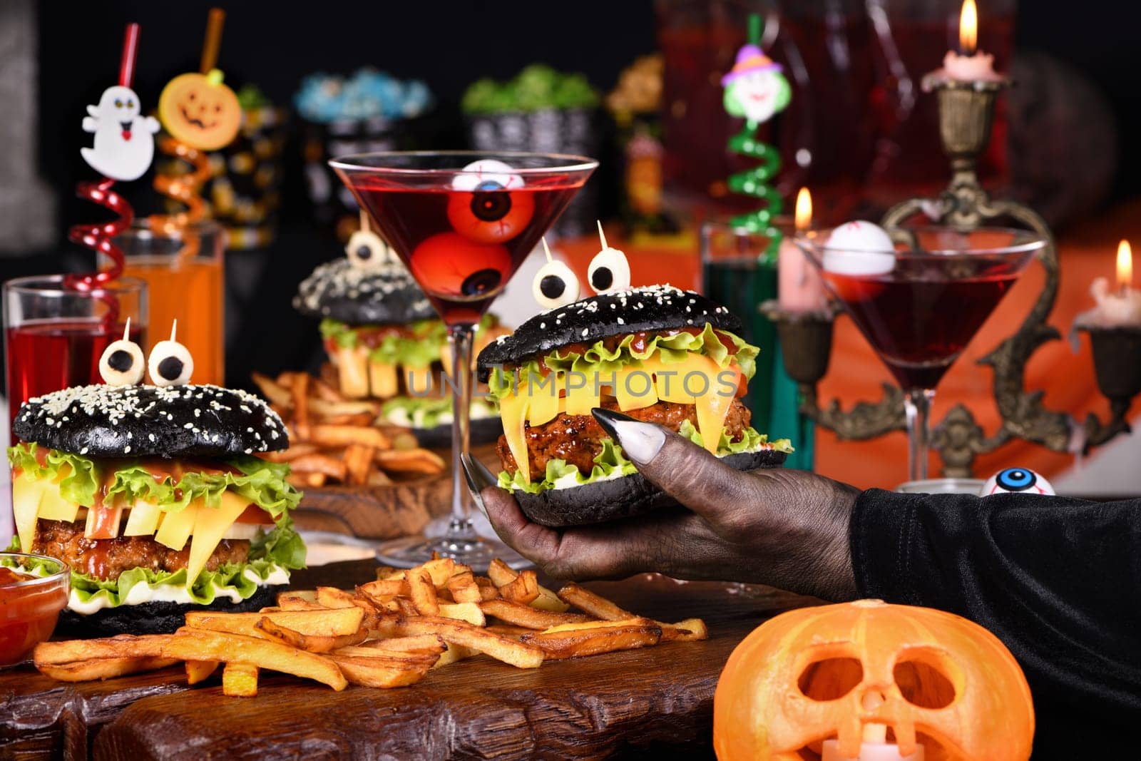  A witch's hand takes a Witch cocktail with eyeballs in a martini glass from the Halloween party table.