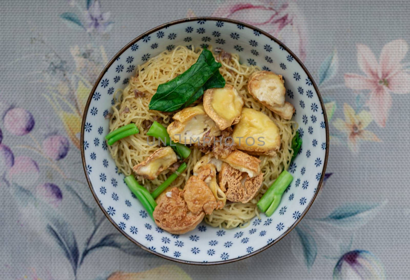 Top view of Egg Noodles with Fried tofu and Chinese kale without Soup sprinkled with Fried garlic in Ceramic bowl. Space for text, Selective focus.