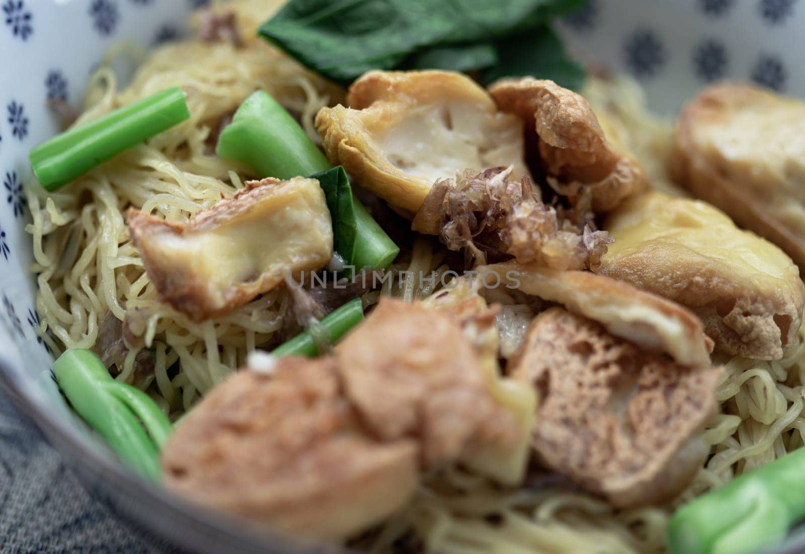 Close-up of Egg Noodles with Fried tofu and Chinese kale without Soup sprinkled with Fried garlic in Ceramic bowl. Space for text, Selective focus.