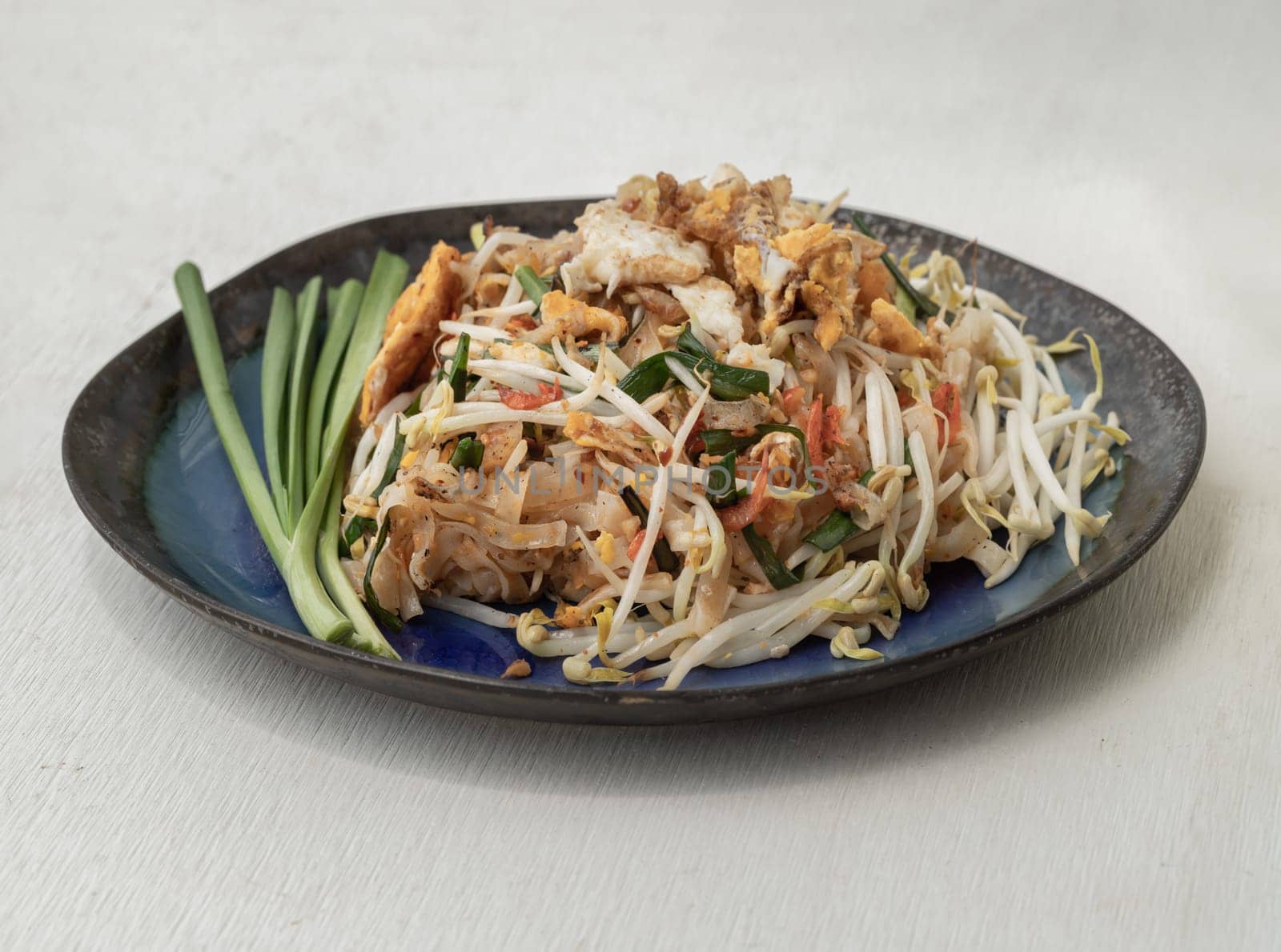 Traditional Fried Thai Noodles (Pad Thai) with Egg, Fried tofu, Dried shrimp, Bean sprouts, Chives and Roasted peanuts on Ceramic plate. That popular food for foreigner tourists. Space for text, Selective focus.