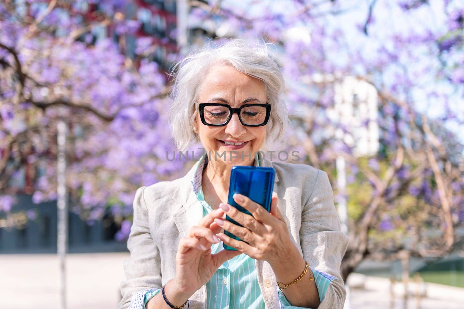 portrait of a lively mature woman smiling happy while typing on mobile phone, concept of technology of communication and modern lifestyle in adulthood, copyspace for text