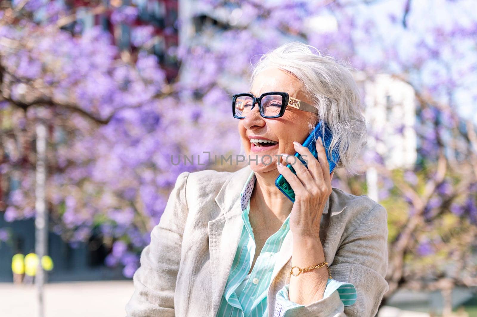 portrait of a lively mature woman laughing happy while talking on mobile phone, concept of technology of communication and modern lifestyle in adulthood, copyspace for text