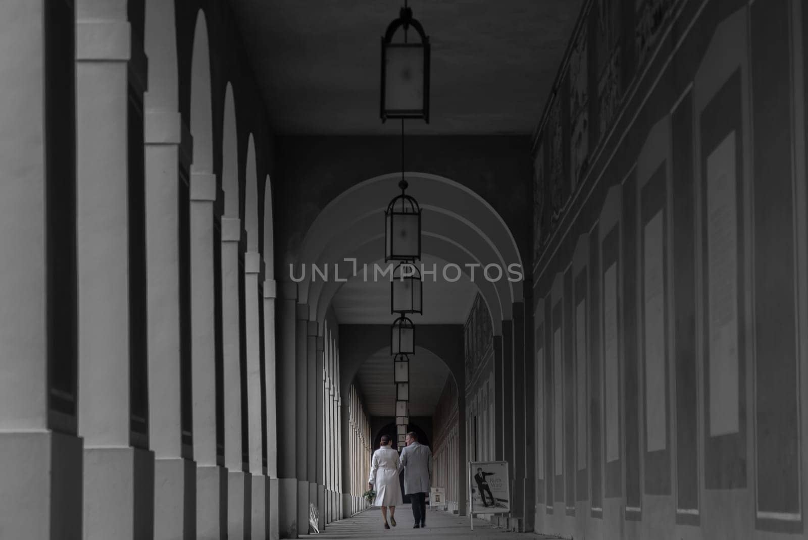 Munich, Germany - Dec 22, 2023 - Couple walks down a Long corridor inside Hofgartenarkaden (Munchen). Both are photographed from behind. Space for text, Selective focus.