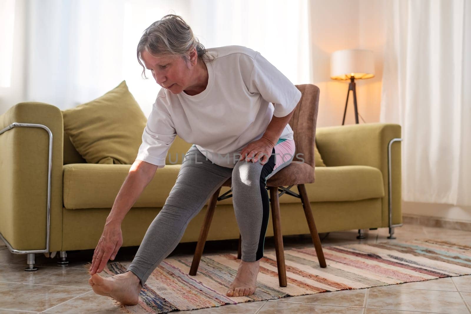 Senior caucasian woman doing doing yoga at home on sofa. stretching legs