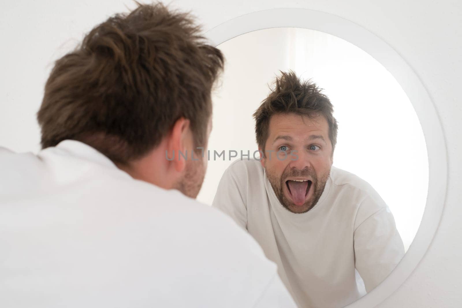 Tired young man is looking at the mirror making funny fces trying to feel better