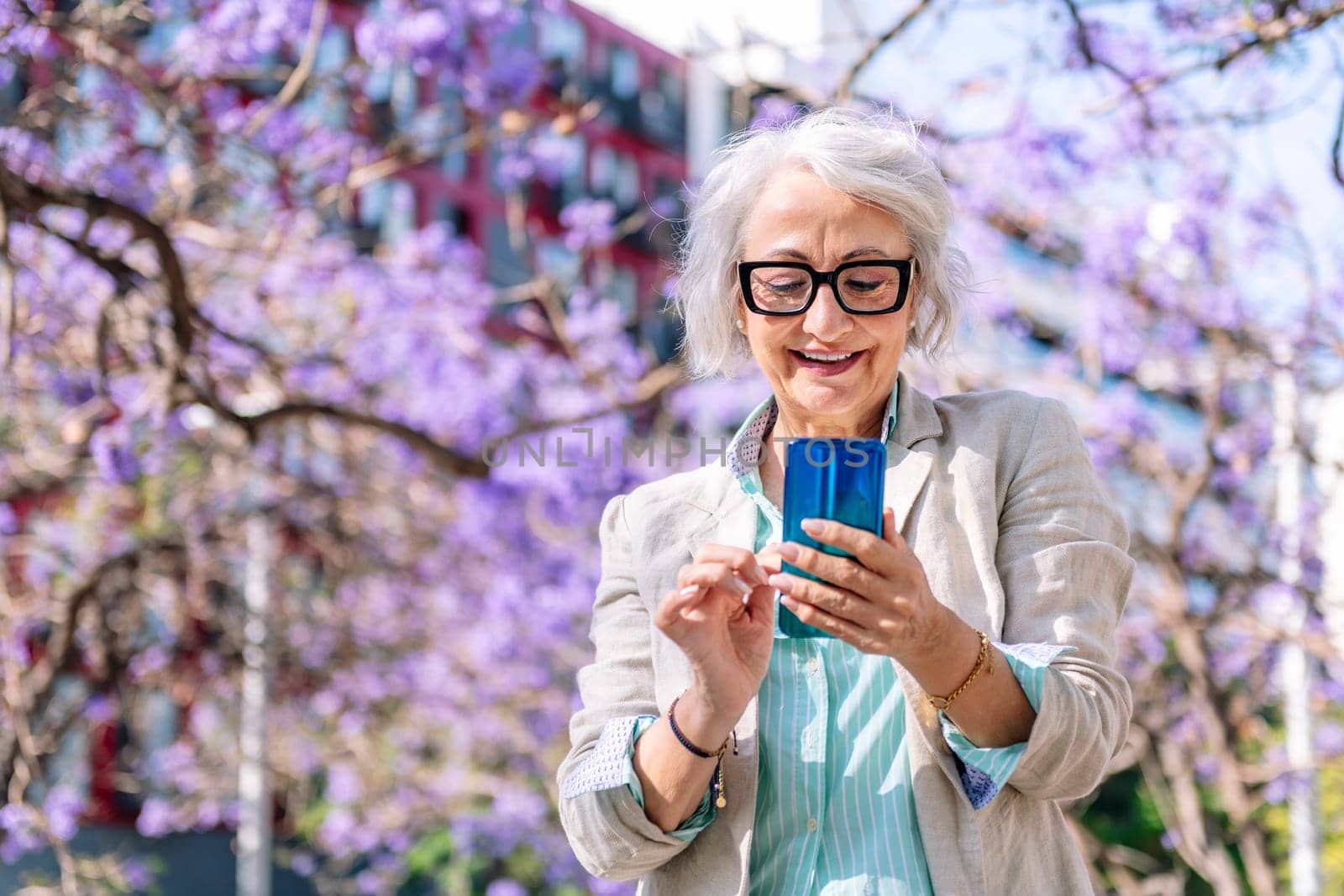 portrait of a lively mature woman smiling happy while typing on mobile phone, concept of technology of communication and modern lifestyle in adulthood, copyspace for text