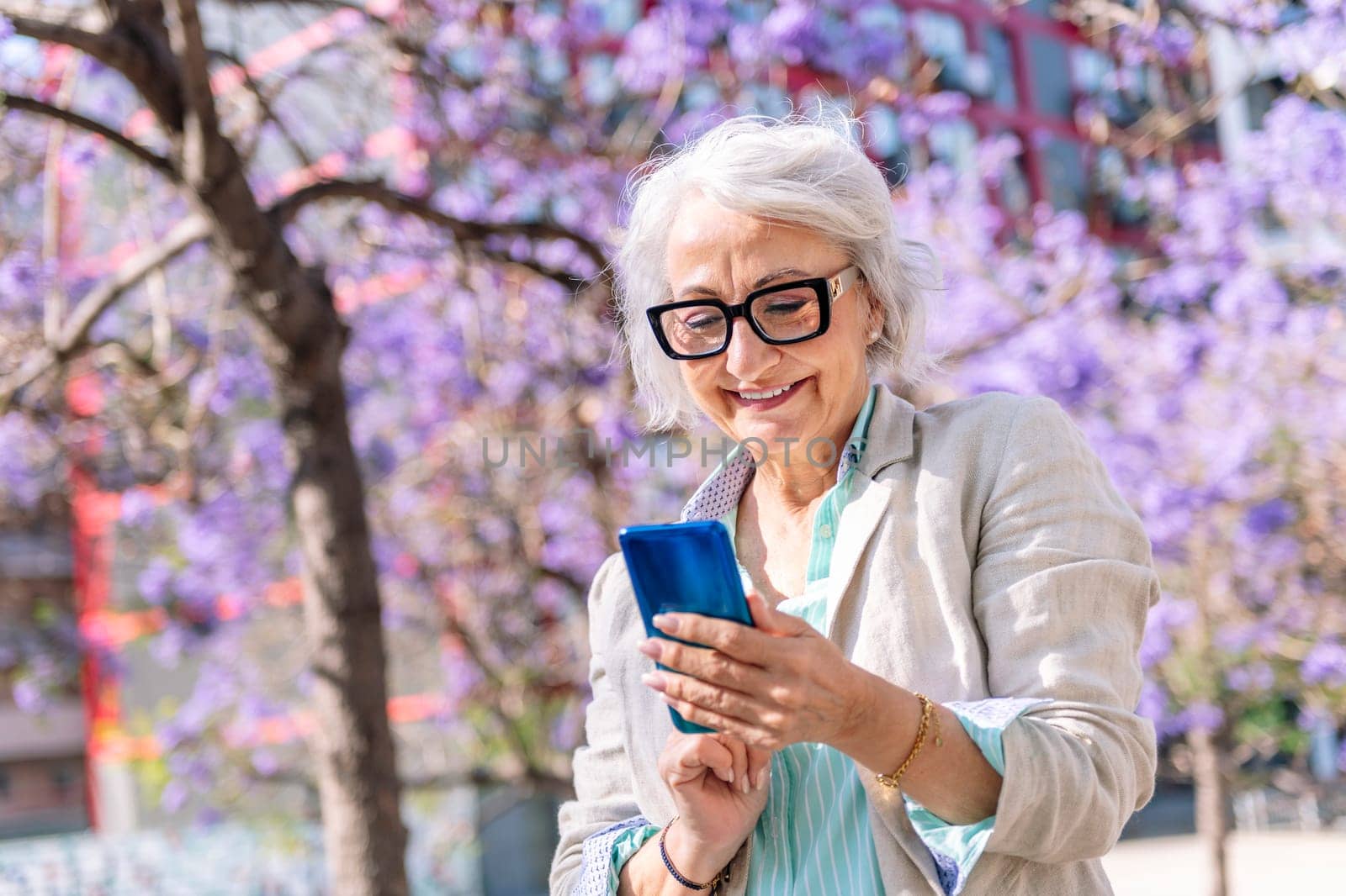 lively mature woman smiling happy while typing on mobile phone, concept of technology of communication and modern lifestyle in adulthood, copyspace for text