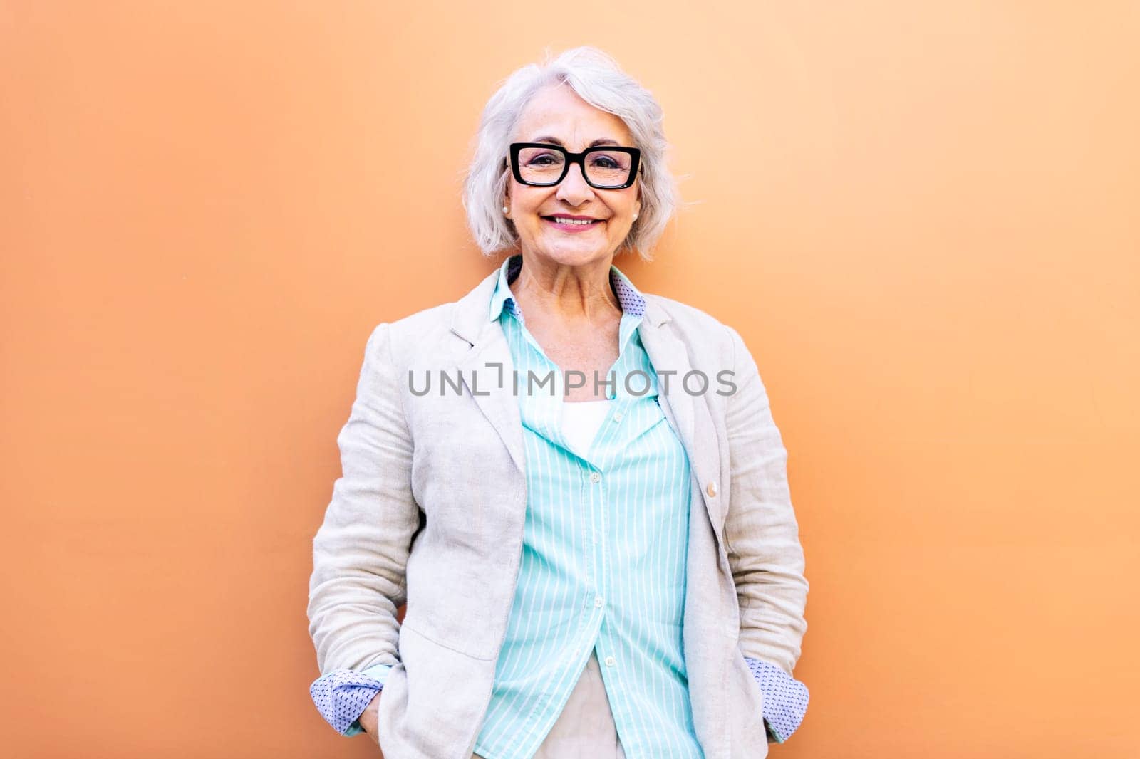 stylish mature entrepreneur woman smiling happy looking at camera leaning on an orange wall, concept of active lifestyle in adulthood, copyspace for text