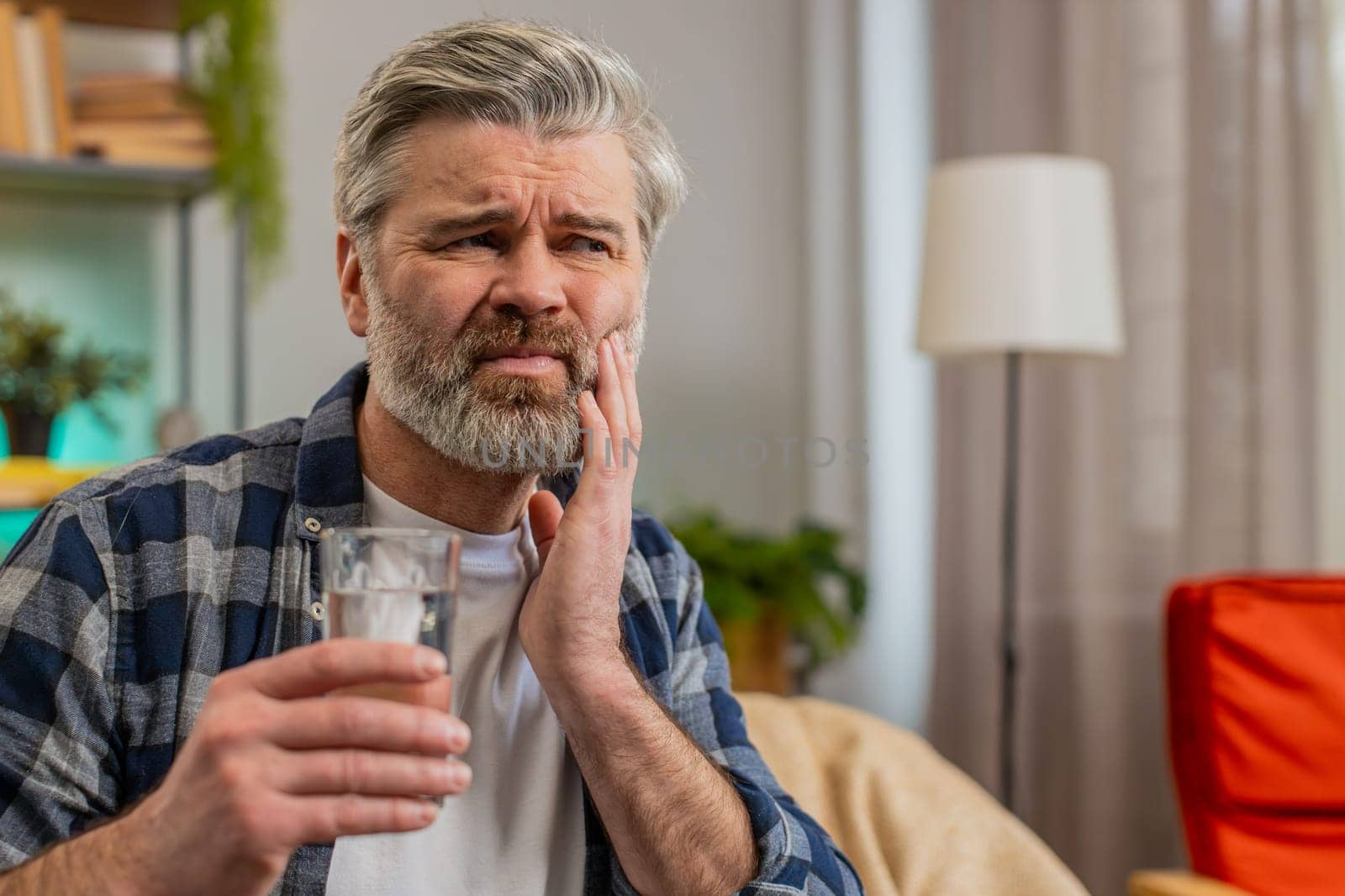 Senior bearded man feel terrible toothache after drink cold water. Middle aged guy sitting in living room touching cheek, feel hurt, suffering from sensitive tooth ache, pain and cavities. Copy-space