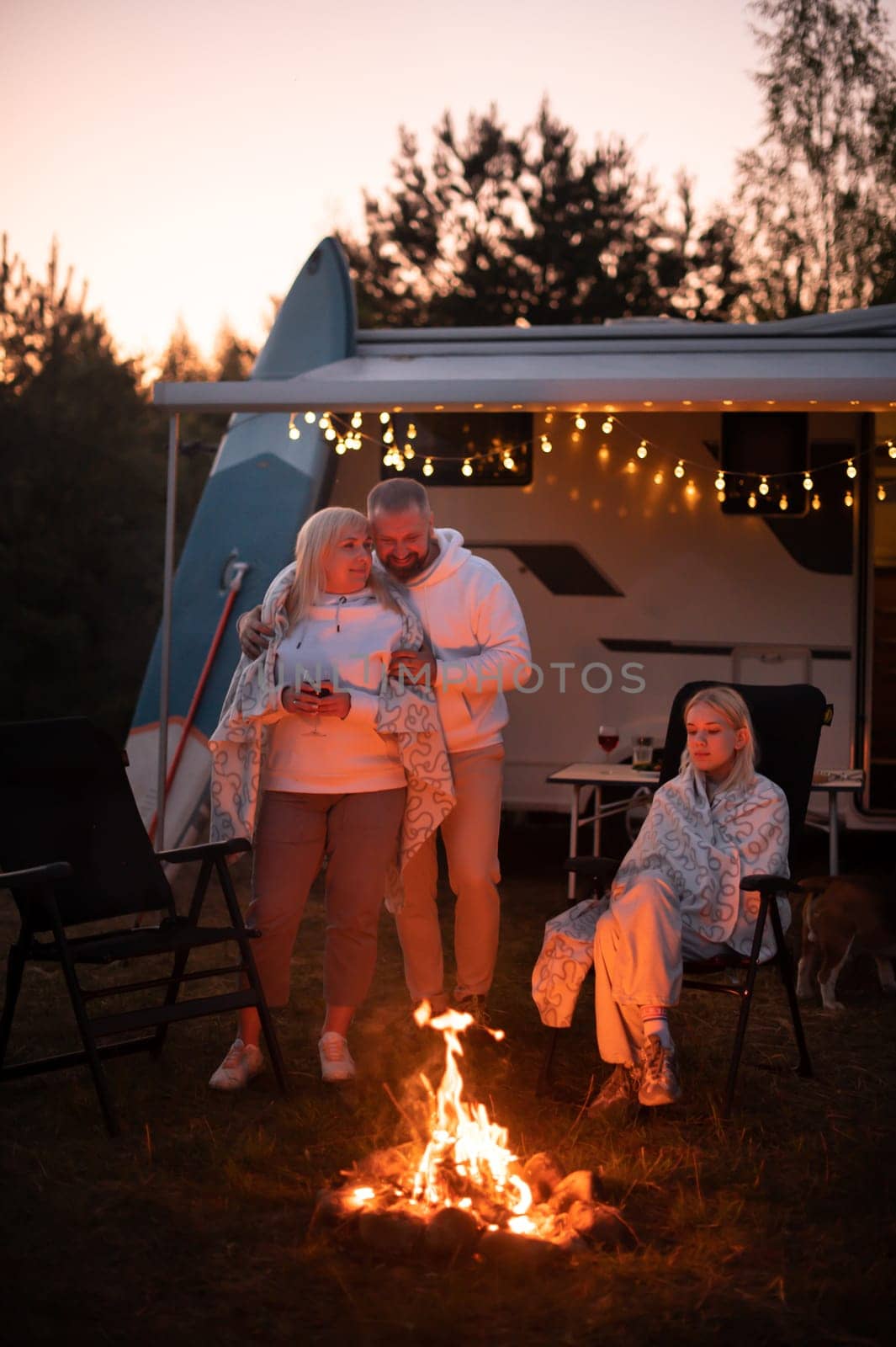 The family is relaxing together by the campfire near their mobile home. Evening family vacation.