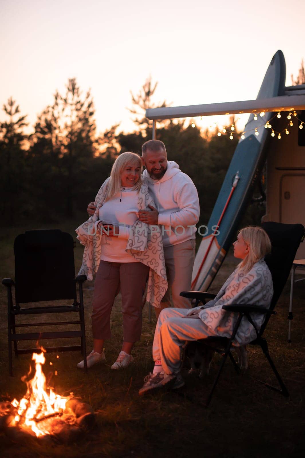 The family is relaxing together by the campfire near their mobile home. Evening family vacation.