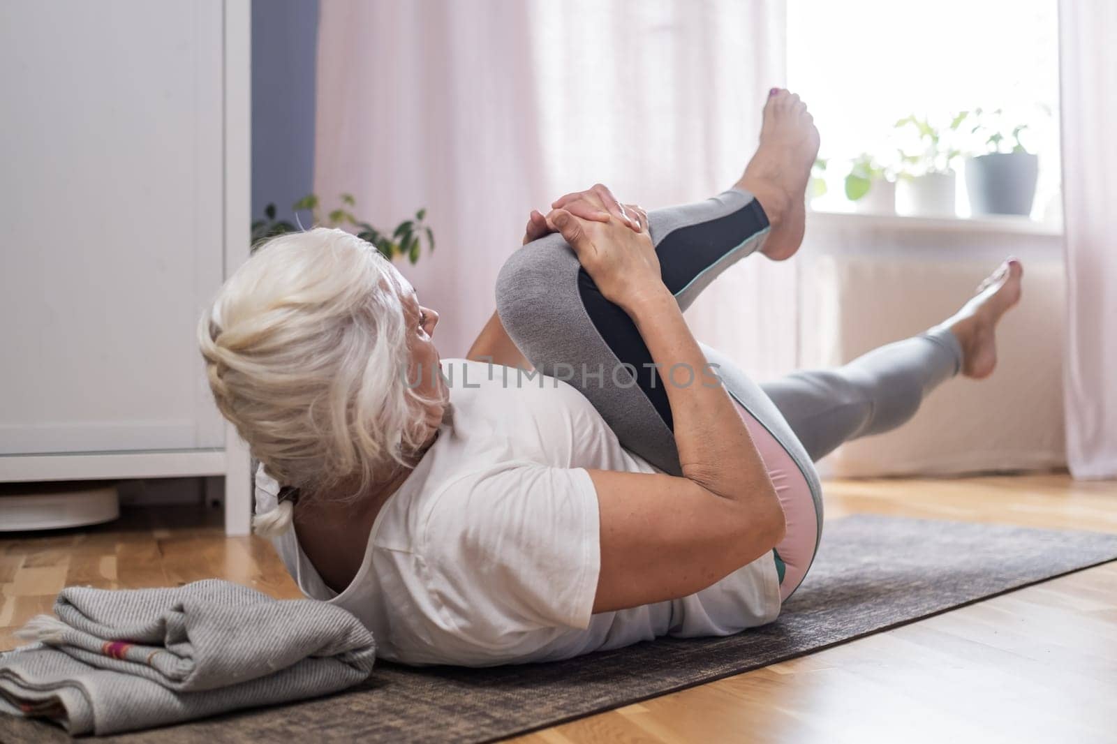 Elderly woman doing pilates on mat in female group at home alone