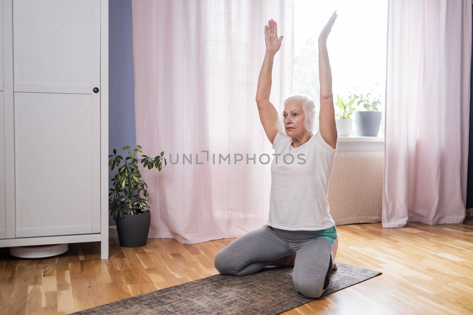 Elderly woman doing pilates on mat in female group at home alone