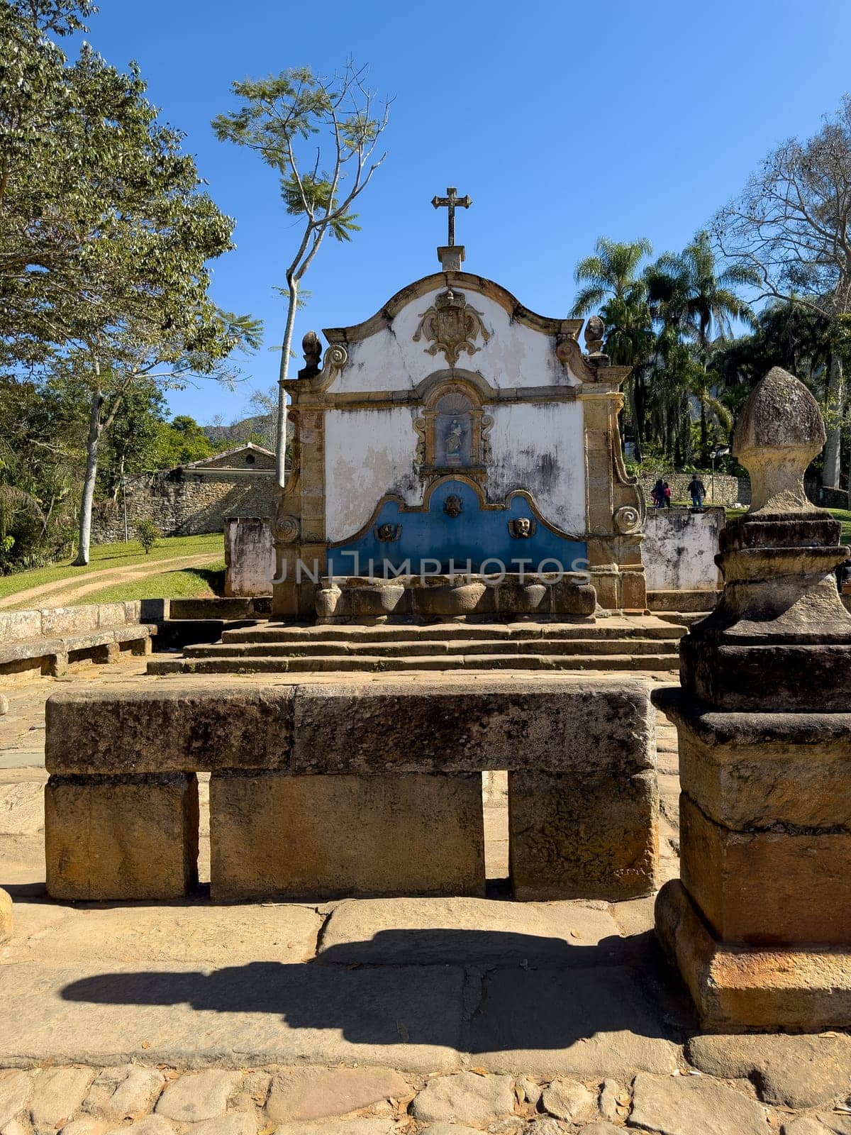 Ancient chapel with a colorful facade stands vividly against a blue sky, surrounded by nature.