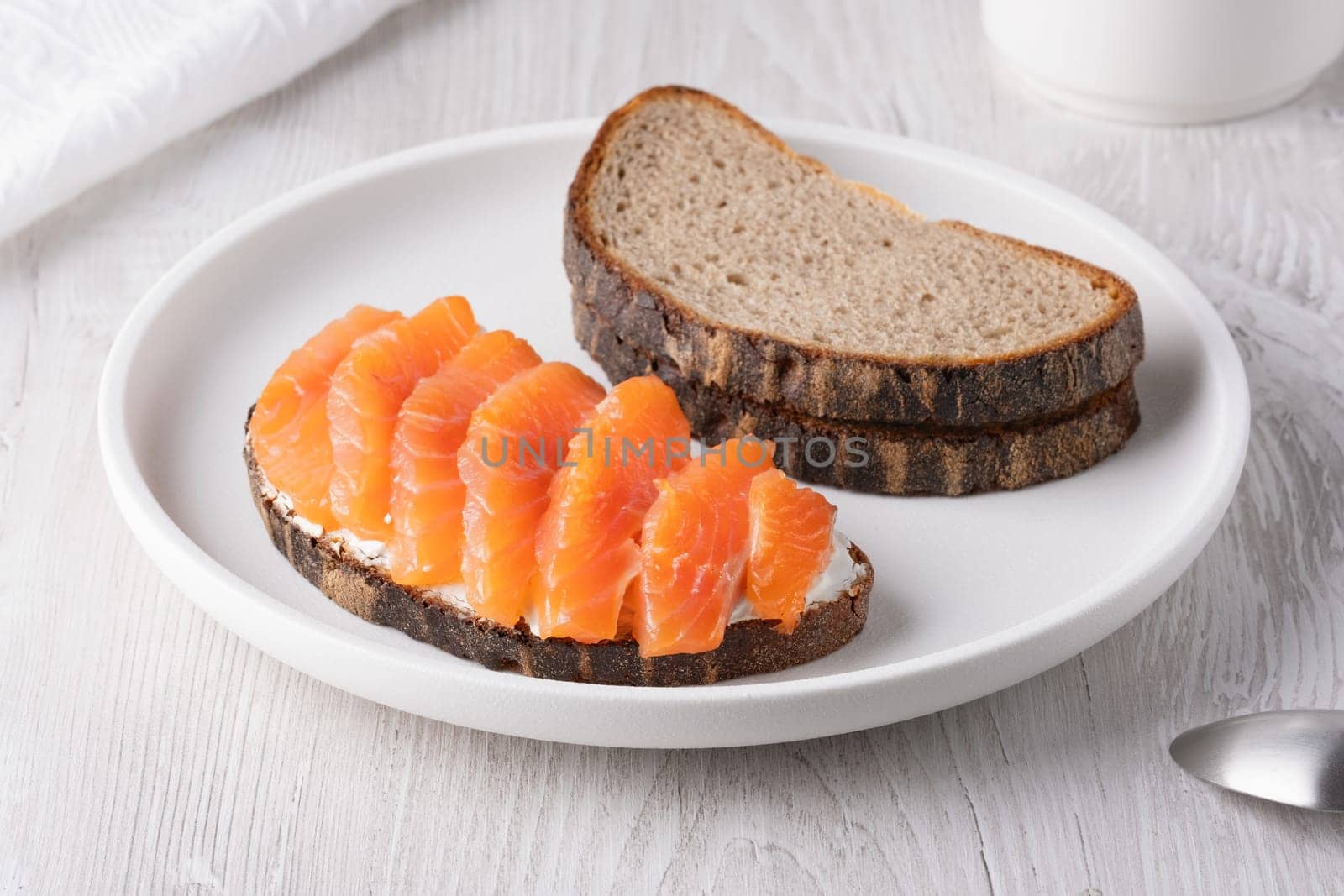 Rye sandwich with salmon and cream cheese on white wooden table.