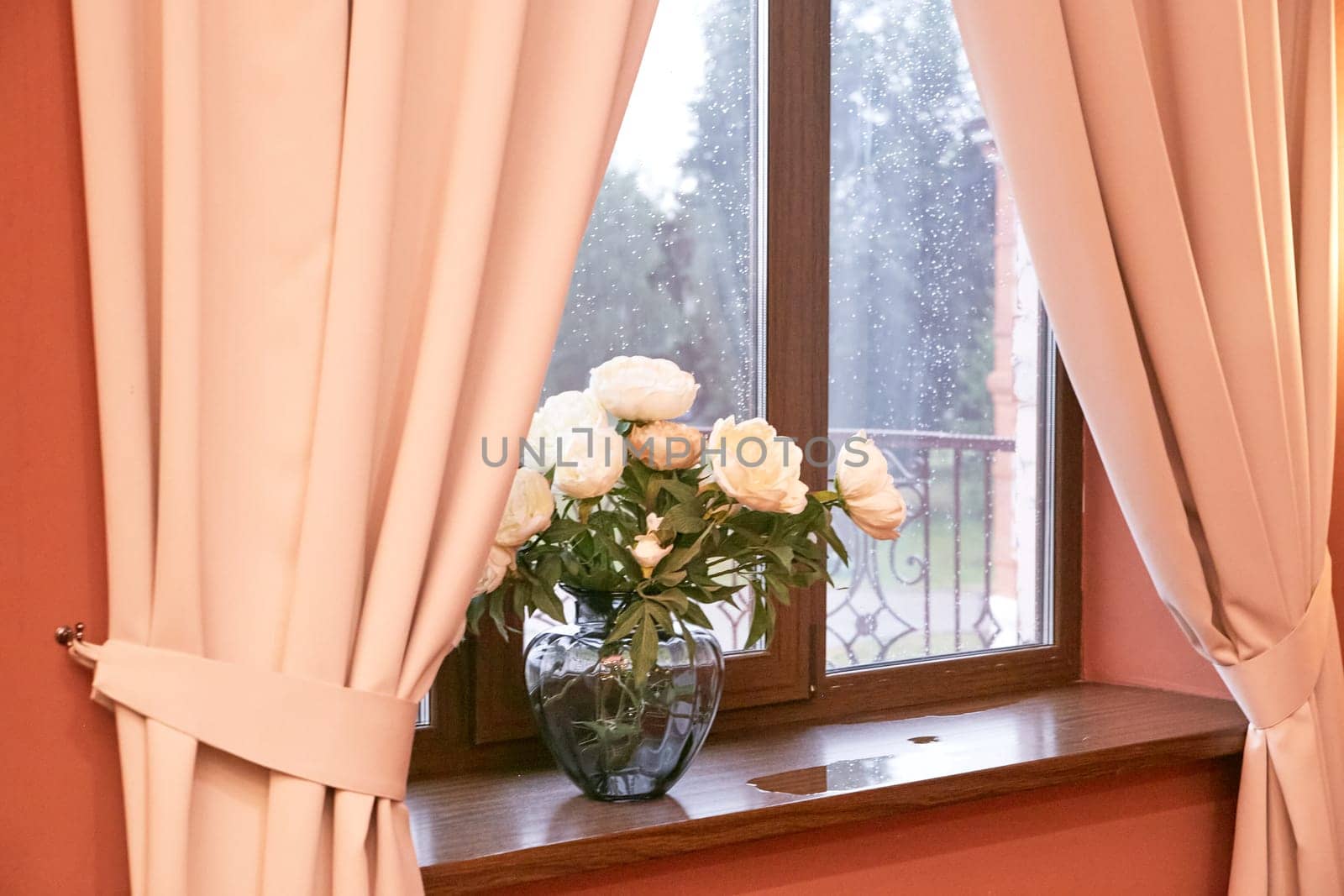 Cream peonies in a glass vase on the window. Flowers at home. Cosiness.
