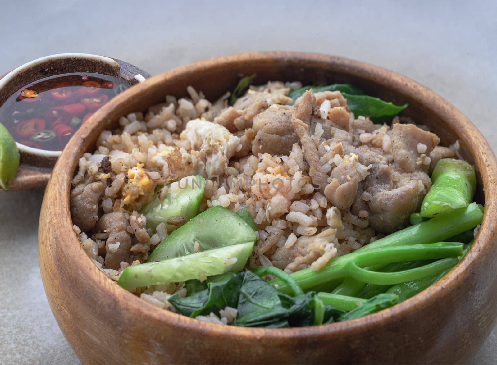 Close-up of Traditional Egg fried rice with Onion, Fried pork, Chinese kale and Sliced ​​cucumber in Wooden bowl served with Thai chilli fish sauce on ceramic tray. Space for text, Selective focus.