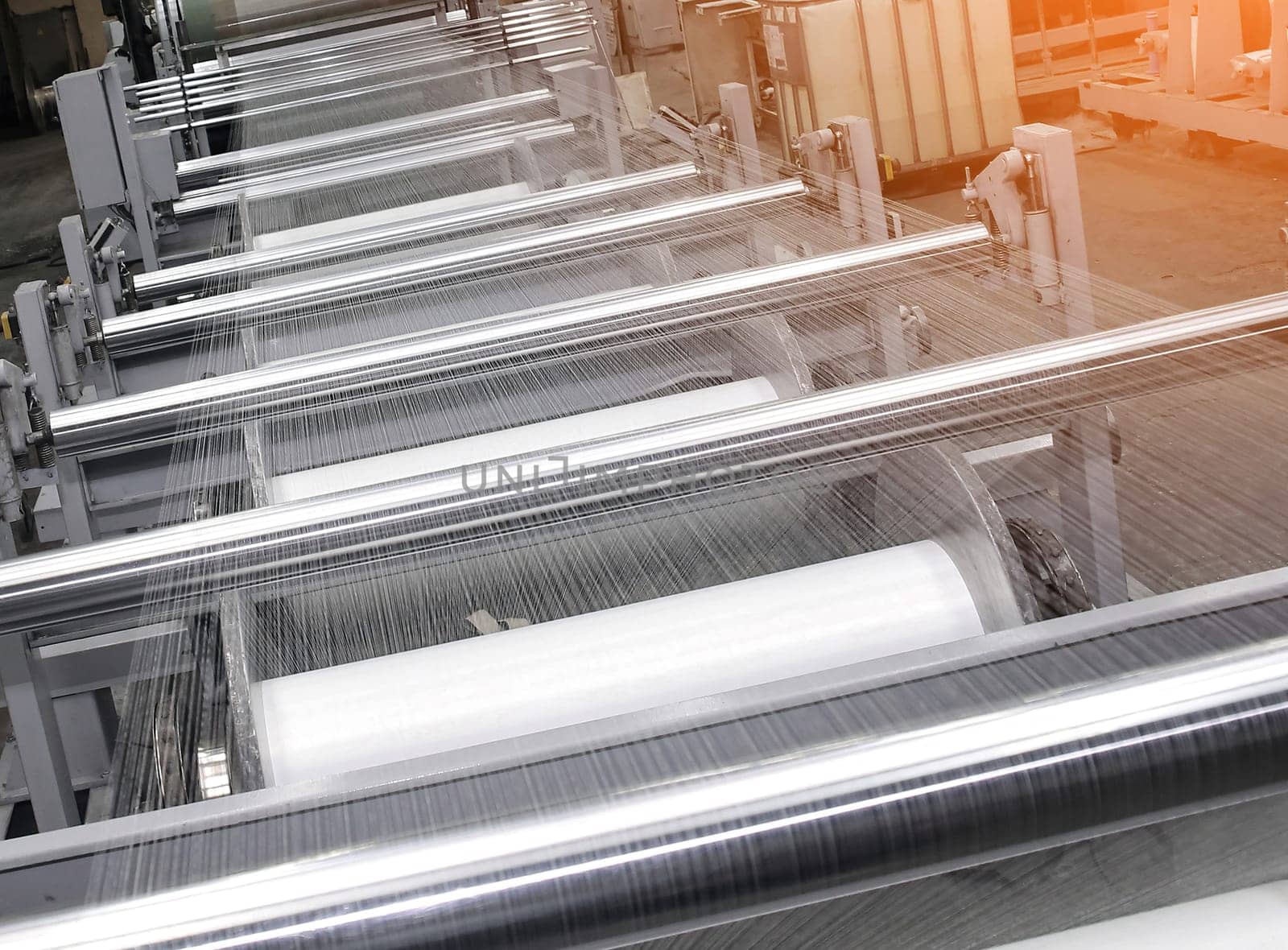 An industrial knitting machine in a textile factory with spools of white thread on a production line. Weaving fabric from yarn in a clean, well-lit manufacturing environment.