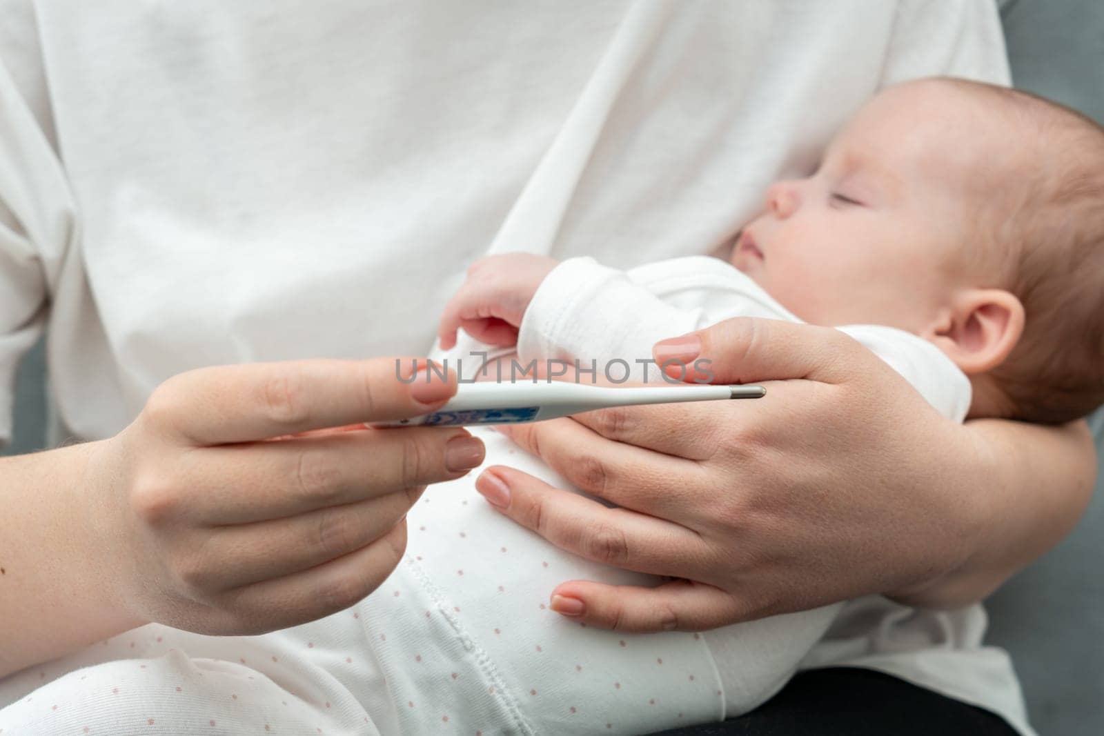 Mother carefully examines thermometer results as she embraces her sick child, ensuring their well