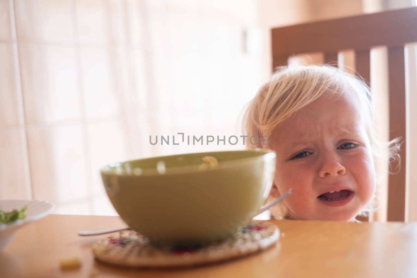Beautiful blond child eating and crying with tantrum at home.. High quality photo
