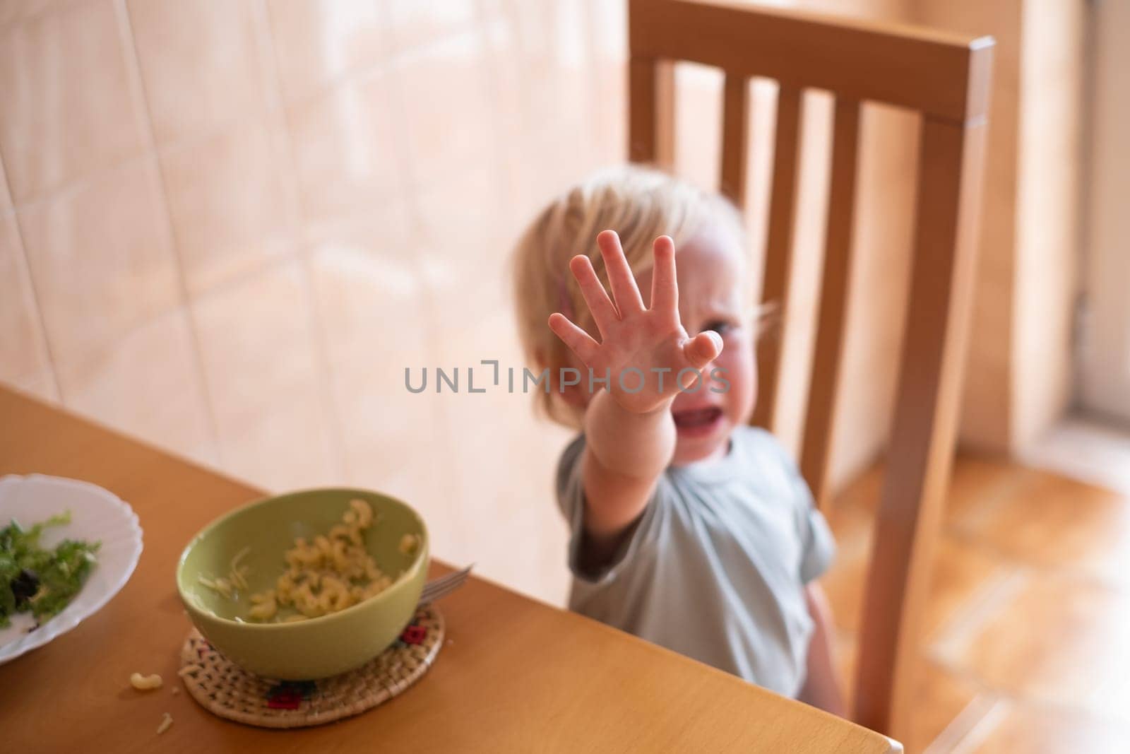 Beautiful blond child eating and crying with tantrum at home.. High quality photo