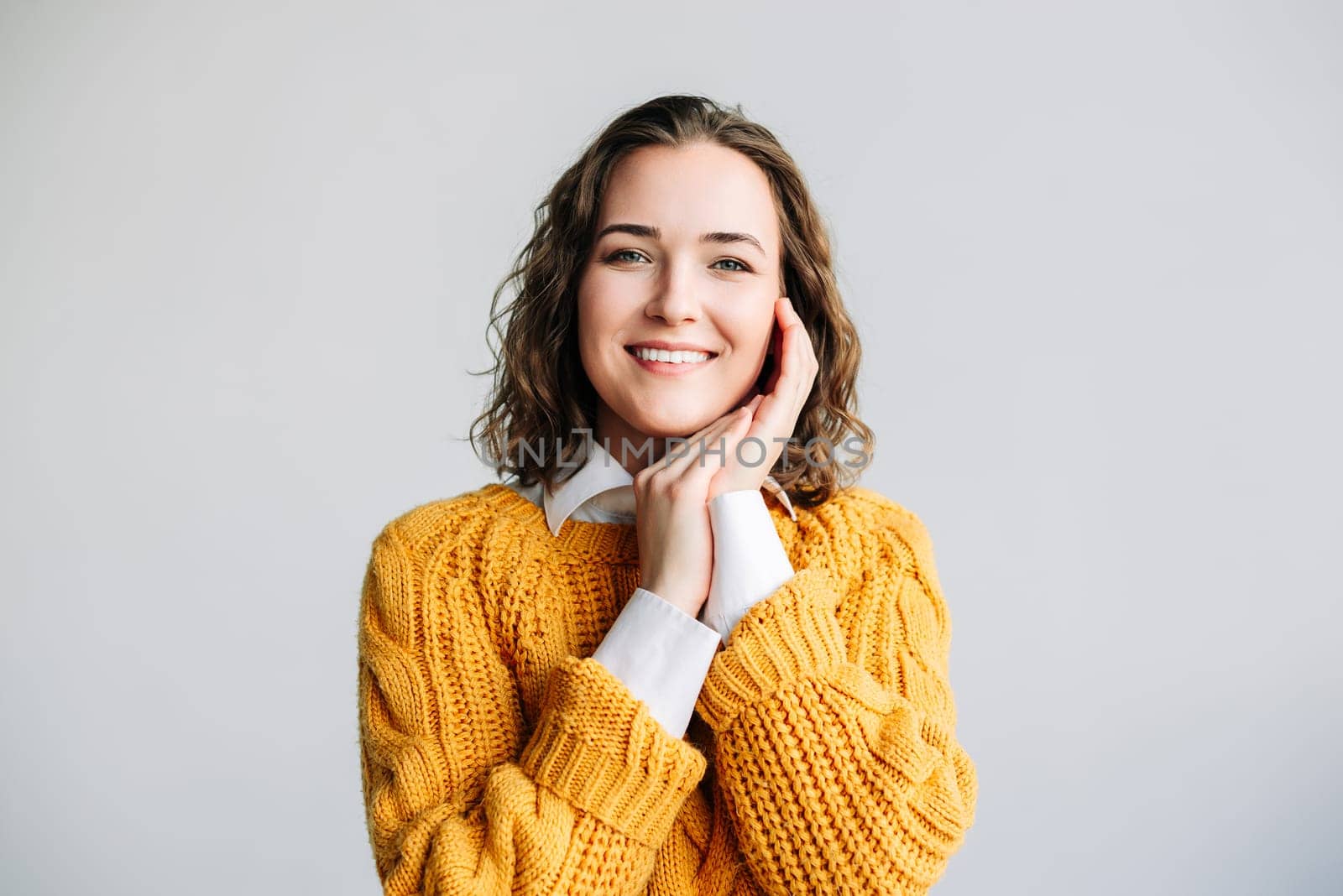 A joyful young woman with curly hair, smiling and looking directly at the camera. Ideal for advertising female products and services. Isolated on a white background, close-up headshot