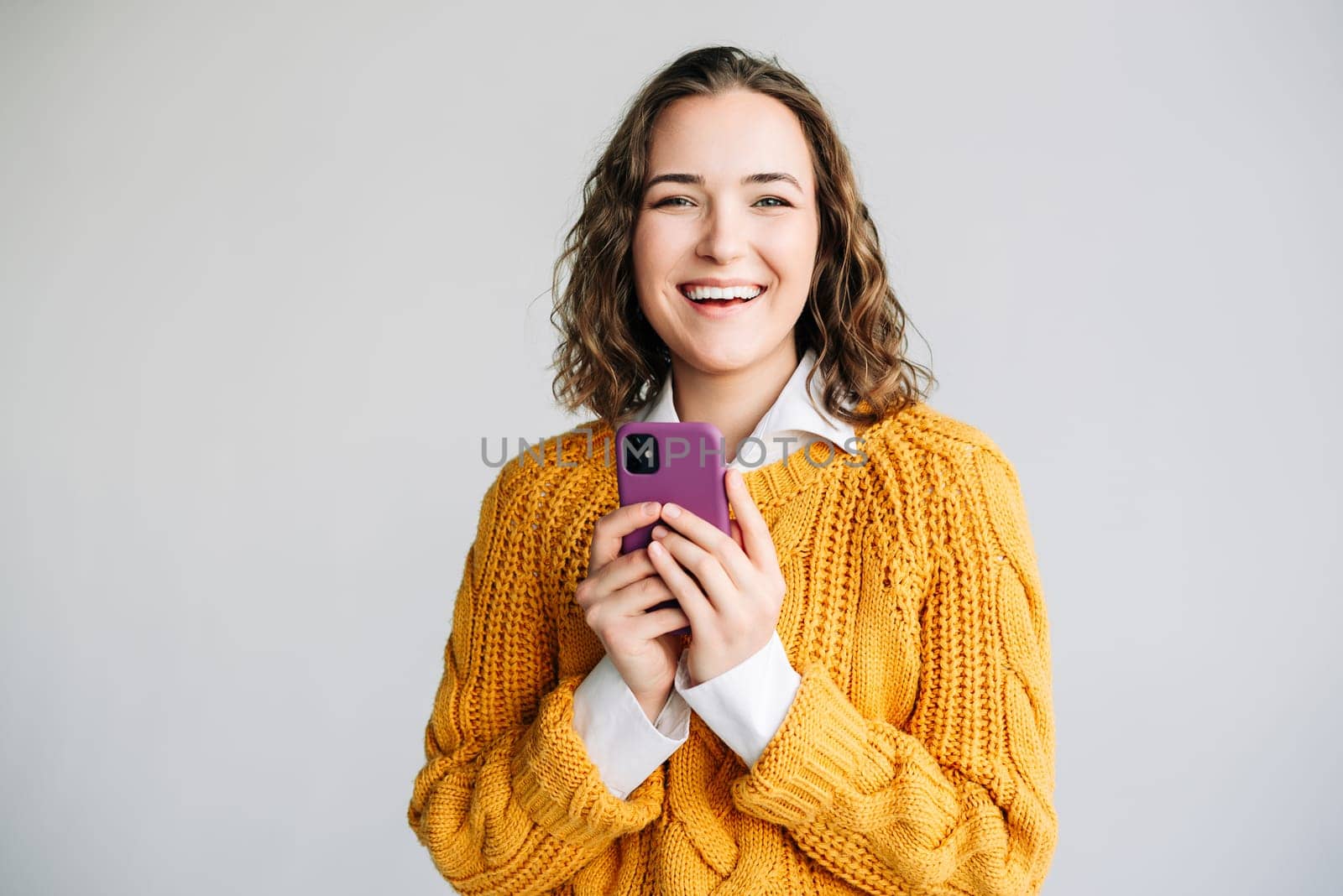 A cheerful young woman holding a smartphone, smiling and looking excited. Perfect for advertising e-commerce, mobile apps, or online communication. Isolated on a white background.