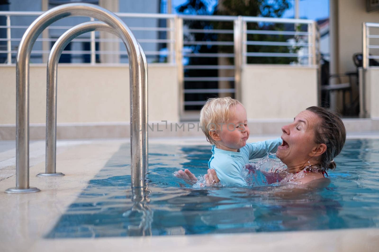 Mother and baby in outdoor swimming pool of tropical resort. Kid learning to swim. Mom and child playing in water. Family summer vacation in exotic destination. Active and healthy sport for kids.
