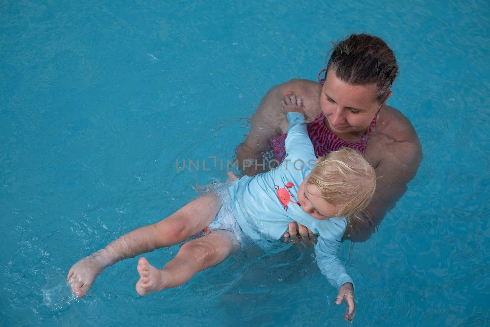 Mother and baby in outdoor swimming pool of tropical resort. Kid learning to swim. Mom and child playing in water. Family summer vacation in exotic destination. Active and healthy sport for kids.