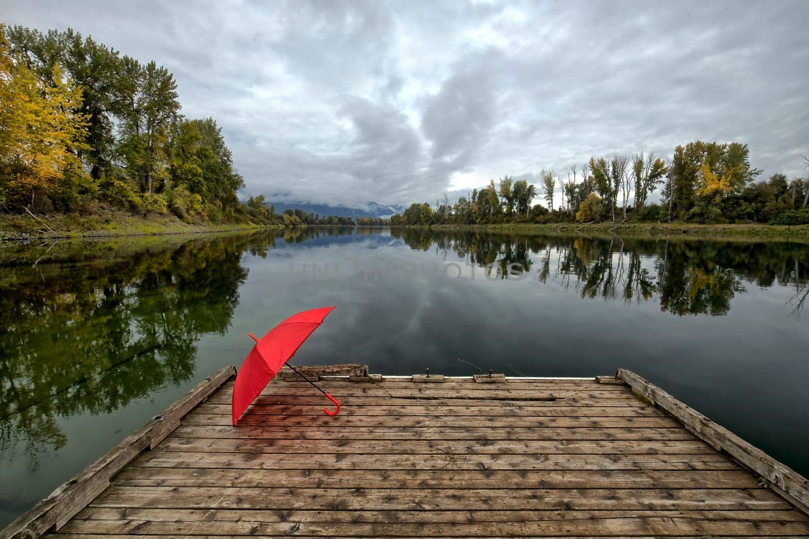 A concept photo of a red umbrella resting on a wooden dock by Kootenai RIver in north Idaho during autumn.