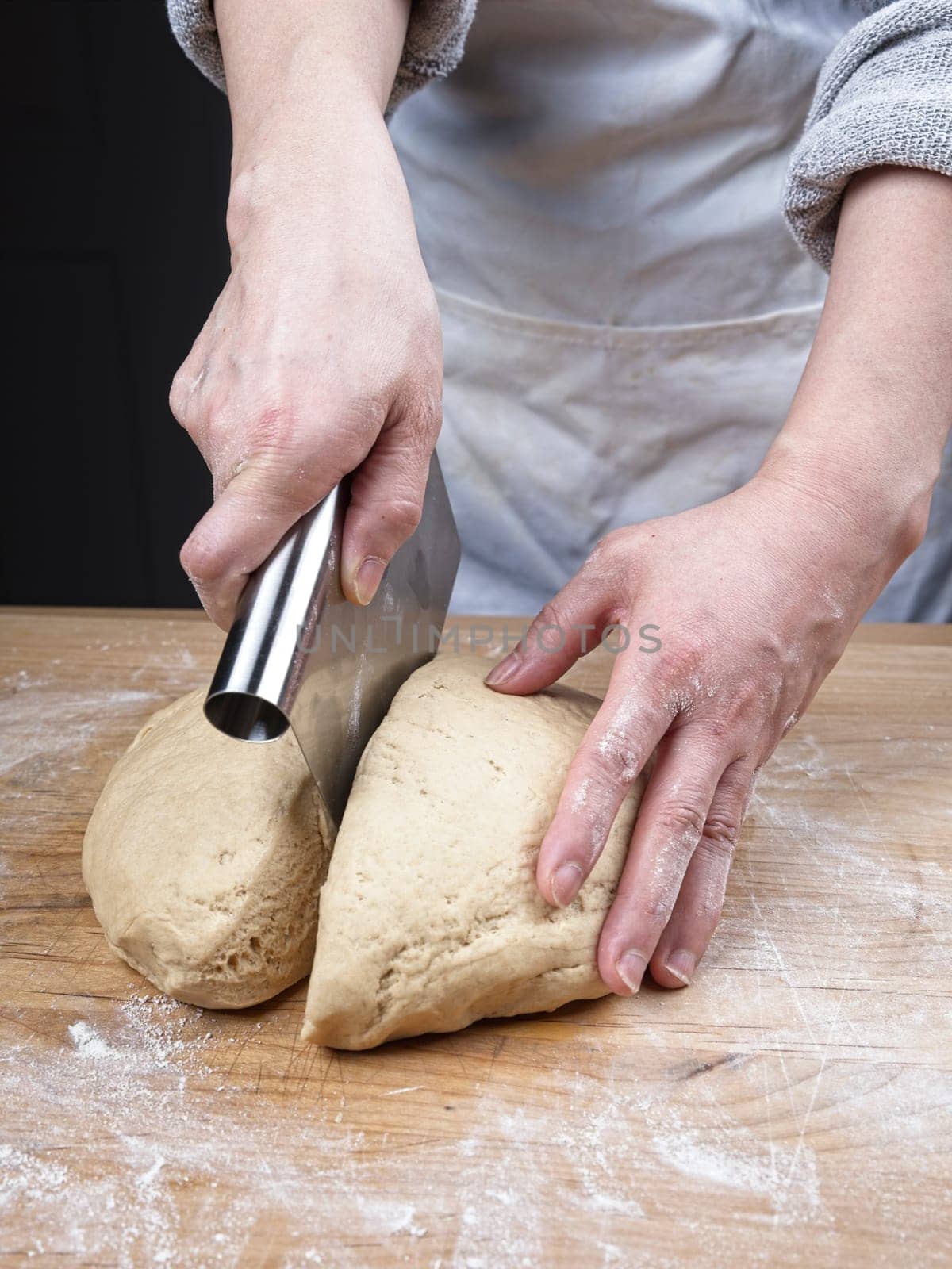 A close up photo of the hands of a woman using a dough cutter to cut a large ball of dough.