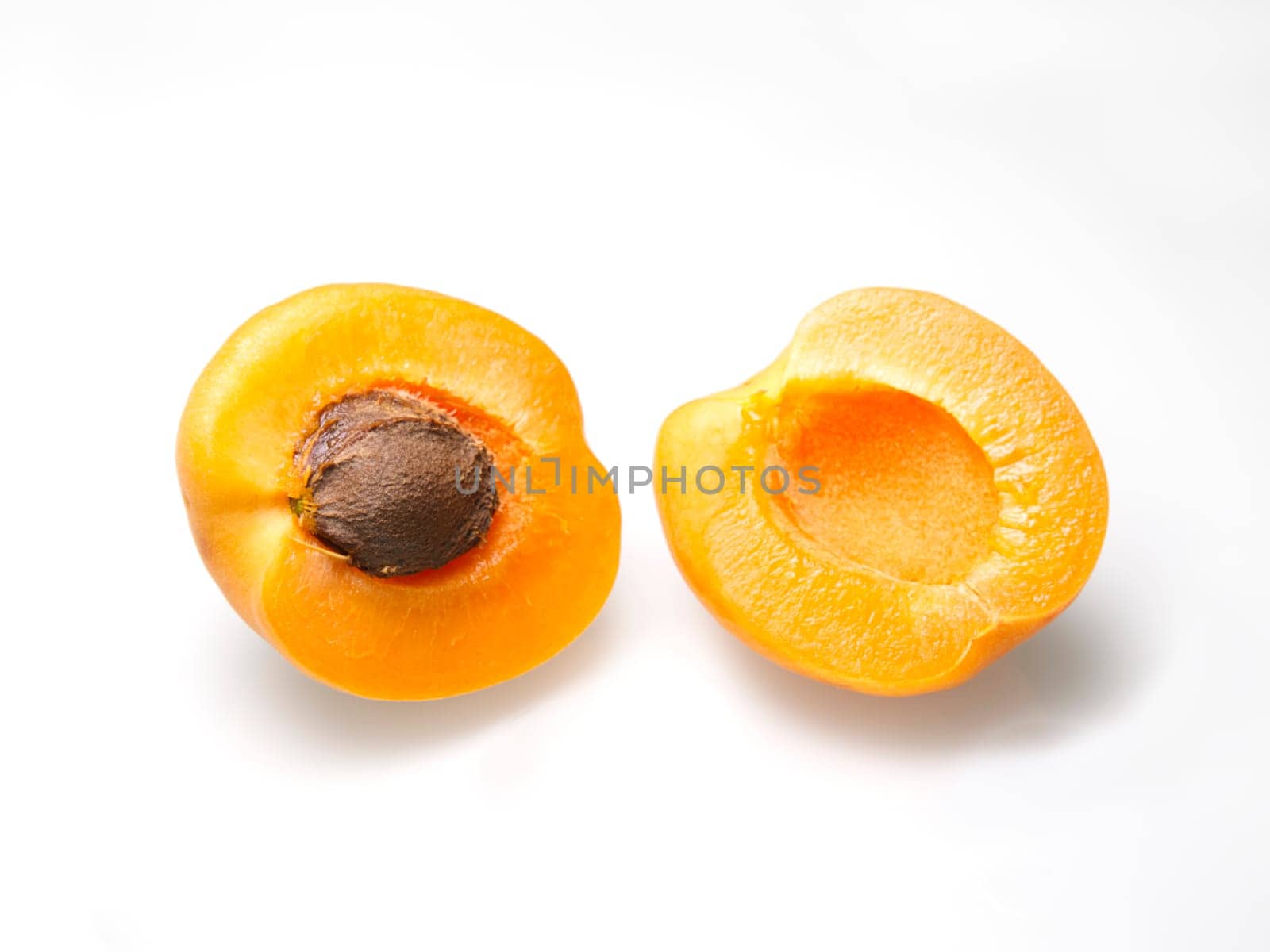 A close up food photo of an apricot cut in half with the pit on a white background.