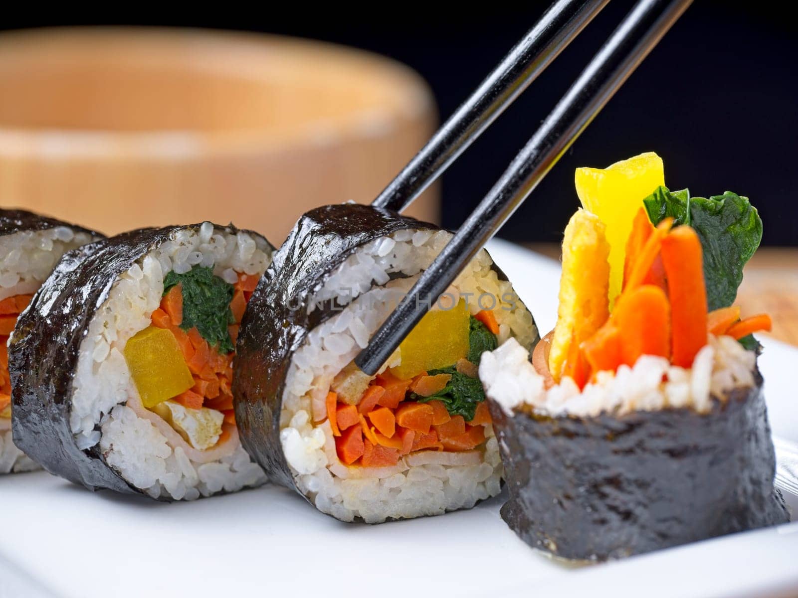 Close up studio photo of Korean kimbap slices displayed on a plate. 