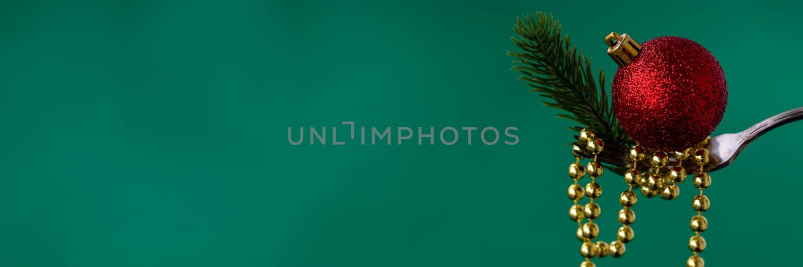 Banner of Christmas decorations on a fork of gold beads, a branch of a Christmas tree and a red Christmas ball on a green background. concept for chinese or oriental new year. copy space