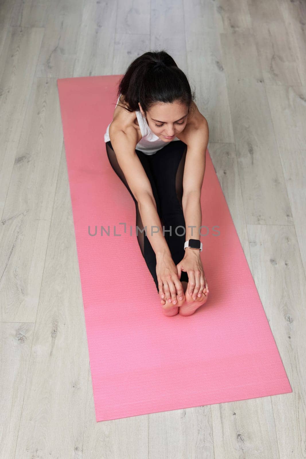 Sporty Caucasian woman worm up by stretching her body on pink exercise mat, top view