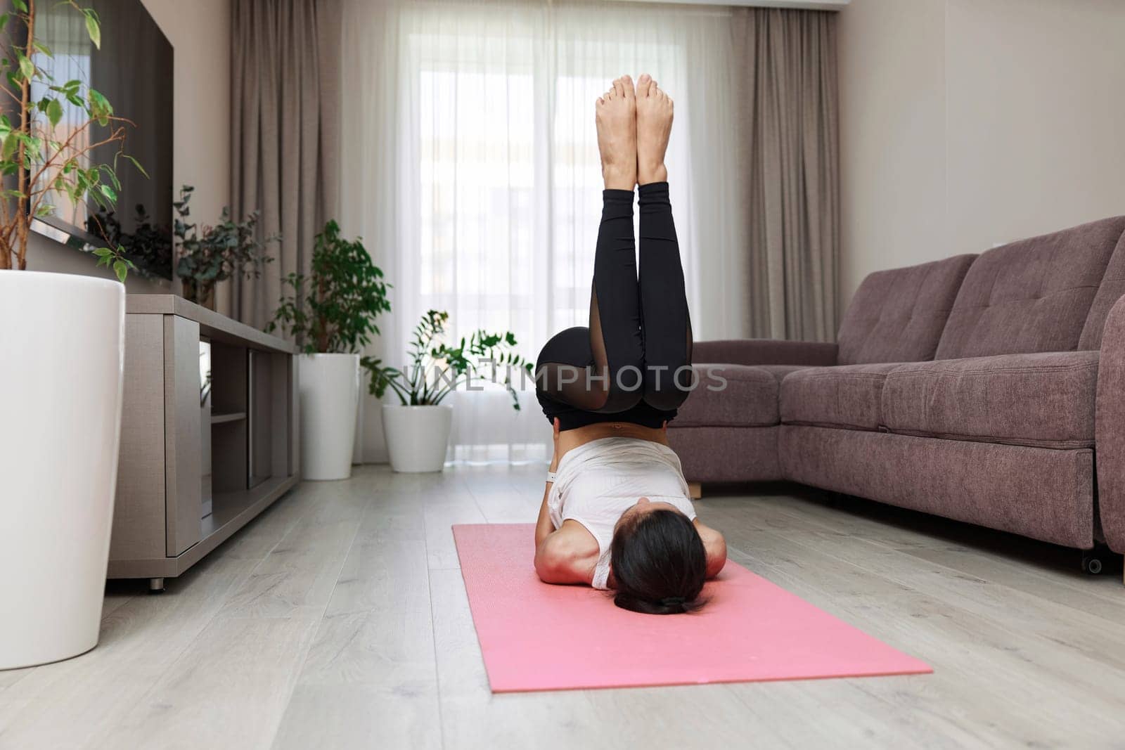 sporty woman working out lying on her back on pink mat lifting body and legs above head at home