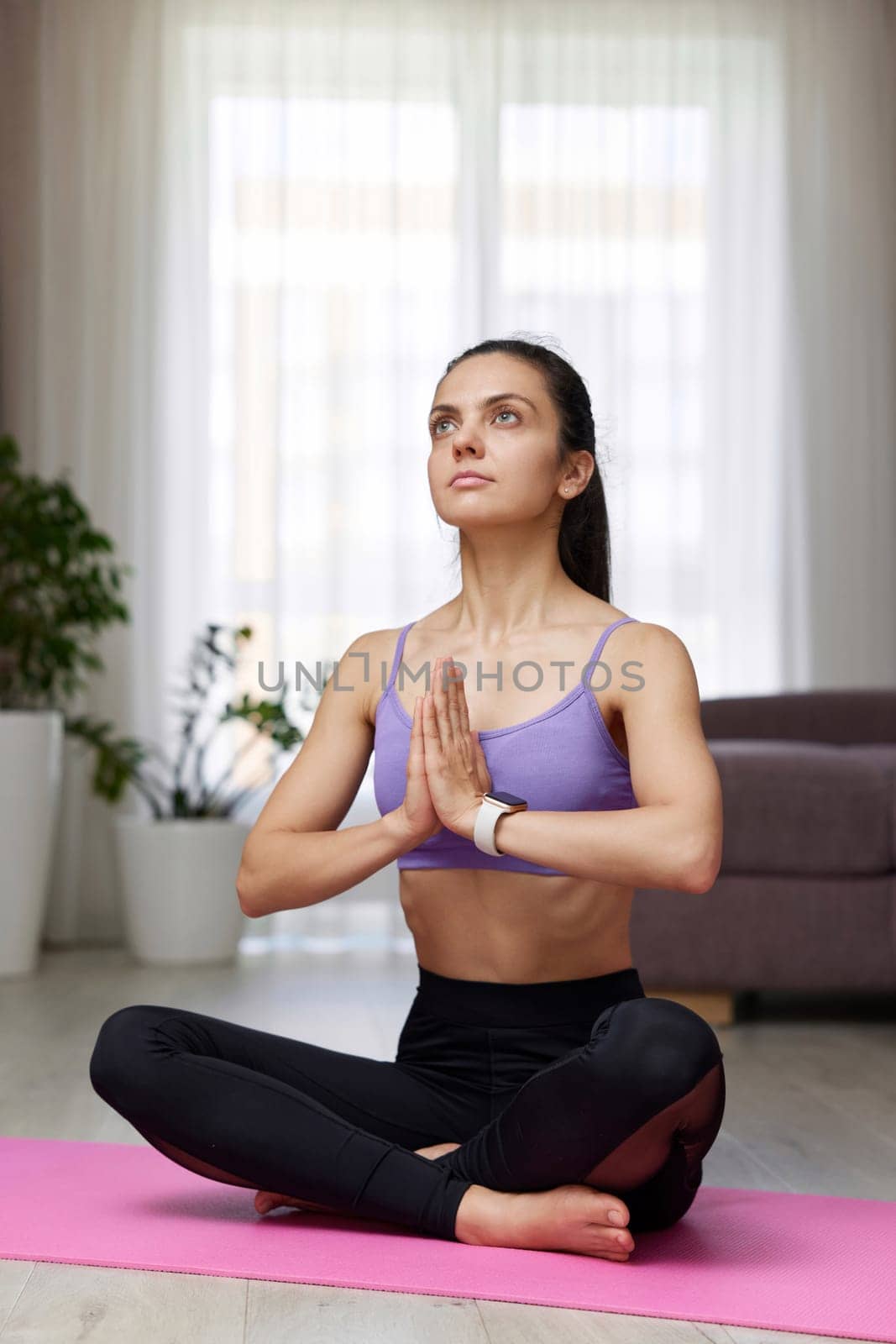 Caucasian woman practicing yoga and meditation sitting in lotus pose on pink yoga mat at home
