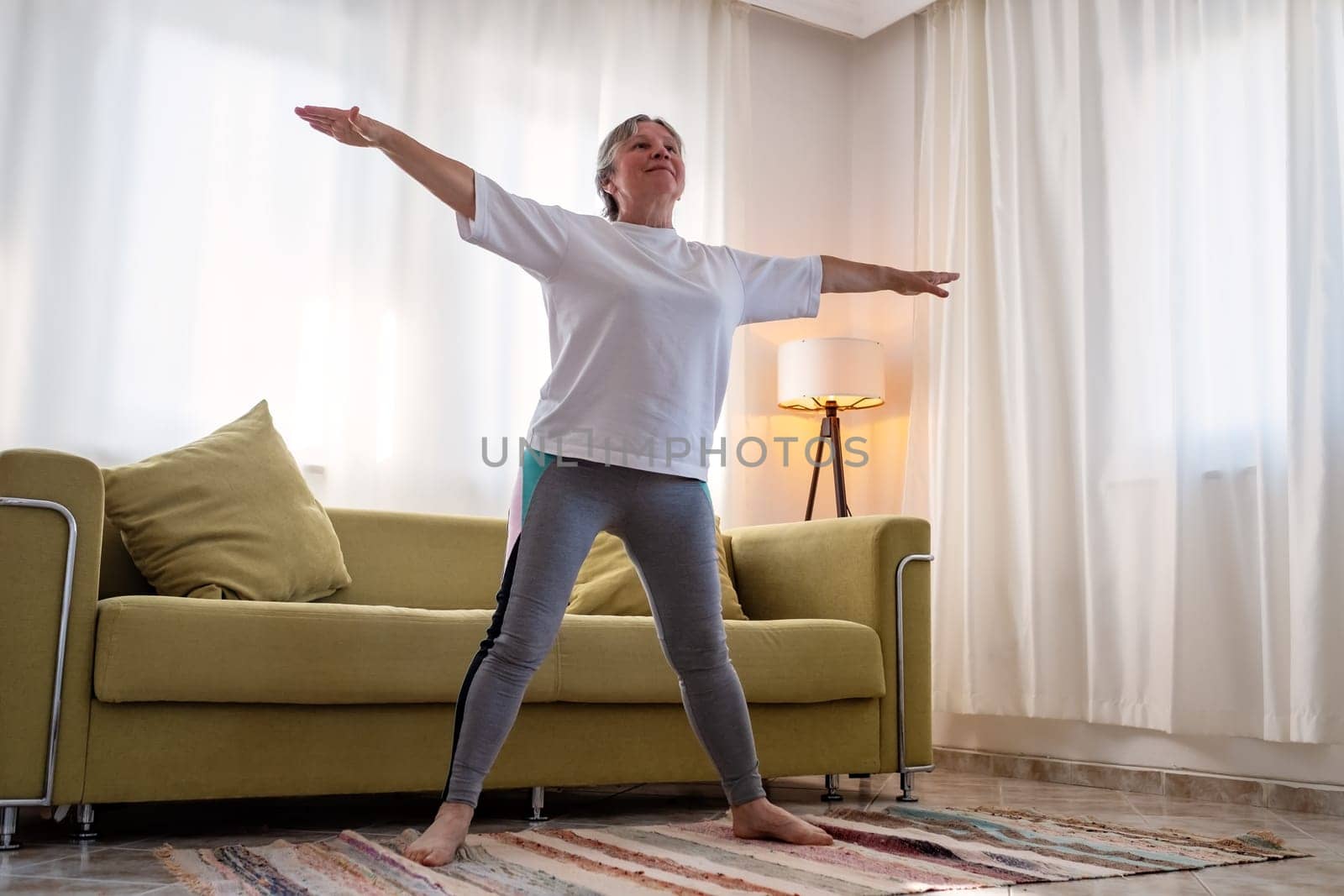 senior woman doing warmup workout at home. Fitness woman doing stretch exercise stretching her body. Elderly woman living an active lifestyle.