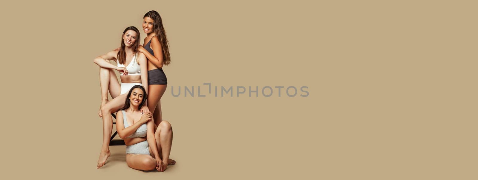 Cheerful calm young arabic, latin and european women in different underwear enjoy natural beauty, body type, isolated on beige background, studio. Fashion, lifestyle, health care, wellness, copy space