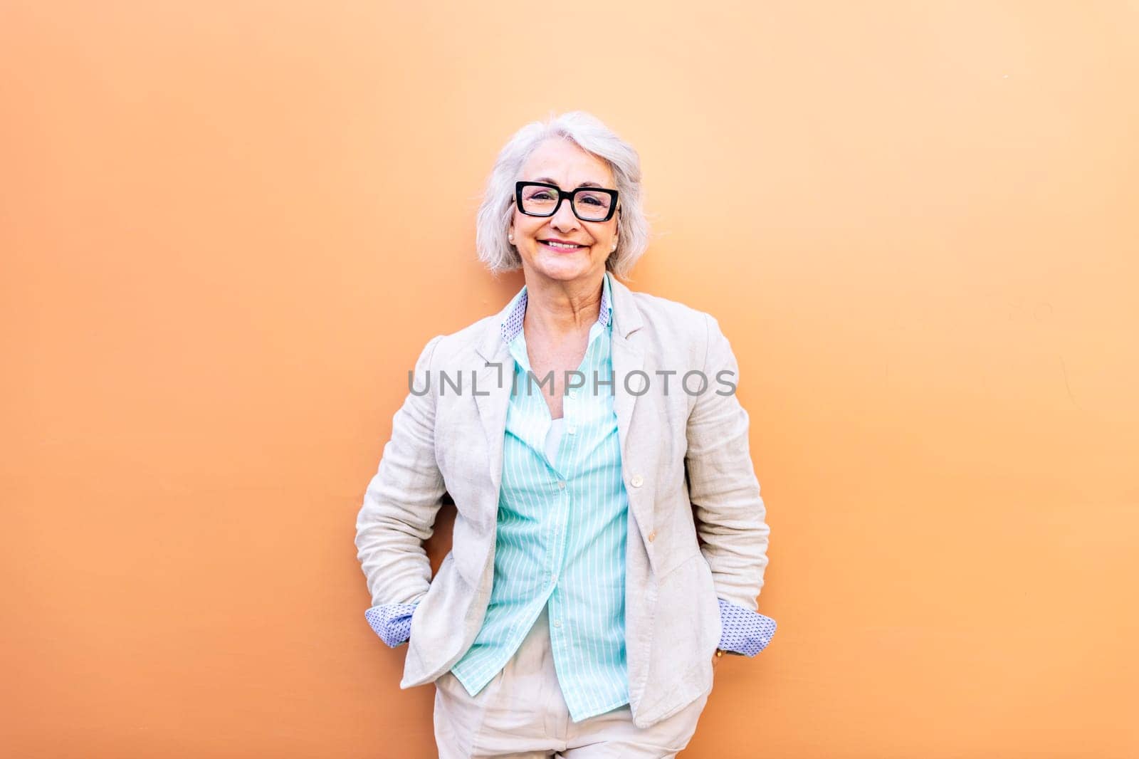 stylish mature woman smiling happy looking at camera leaning on an orange wall, concept of active lifestyle in adulthood, copyspace for text