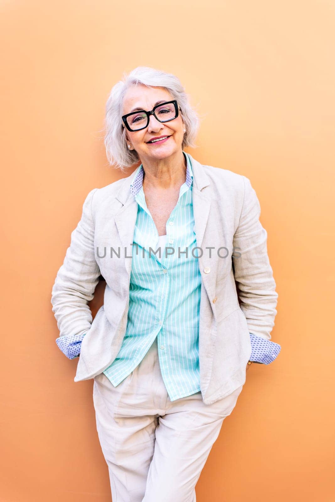 stylish mature entrepreneur woman smiling happy looking at camera leaning on an orange wall, concept of active lifestyle in adulthood, copyspace for text