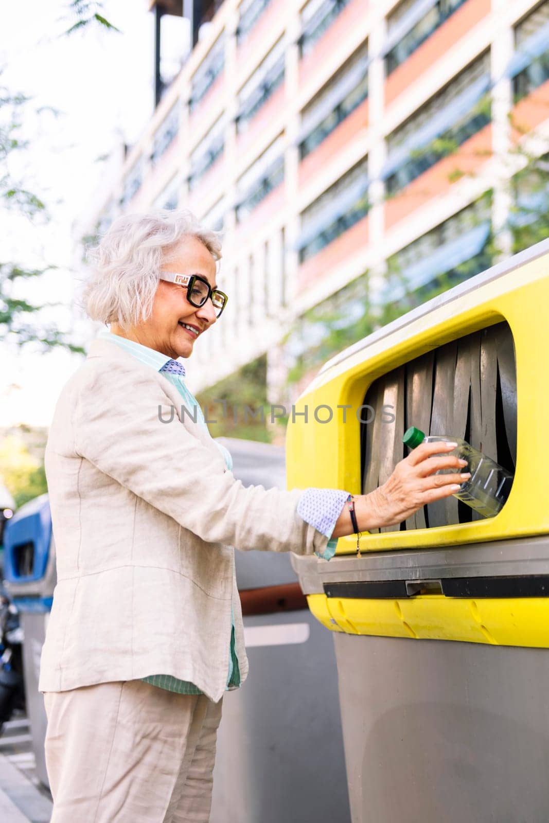 smiling mature woman throwing plastic into recycling bin, concept of sustainability and eco lifestyle