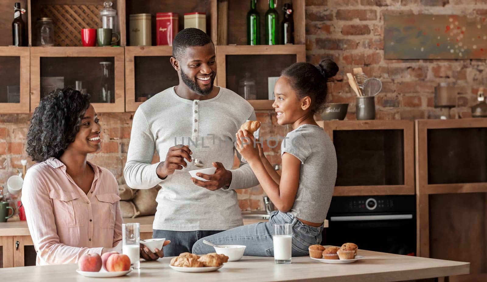 Positive african american family having breakfast in beautiful kitchen, talking while eating, free space