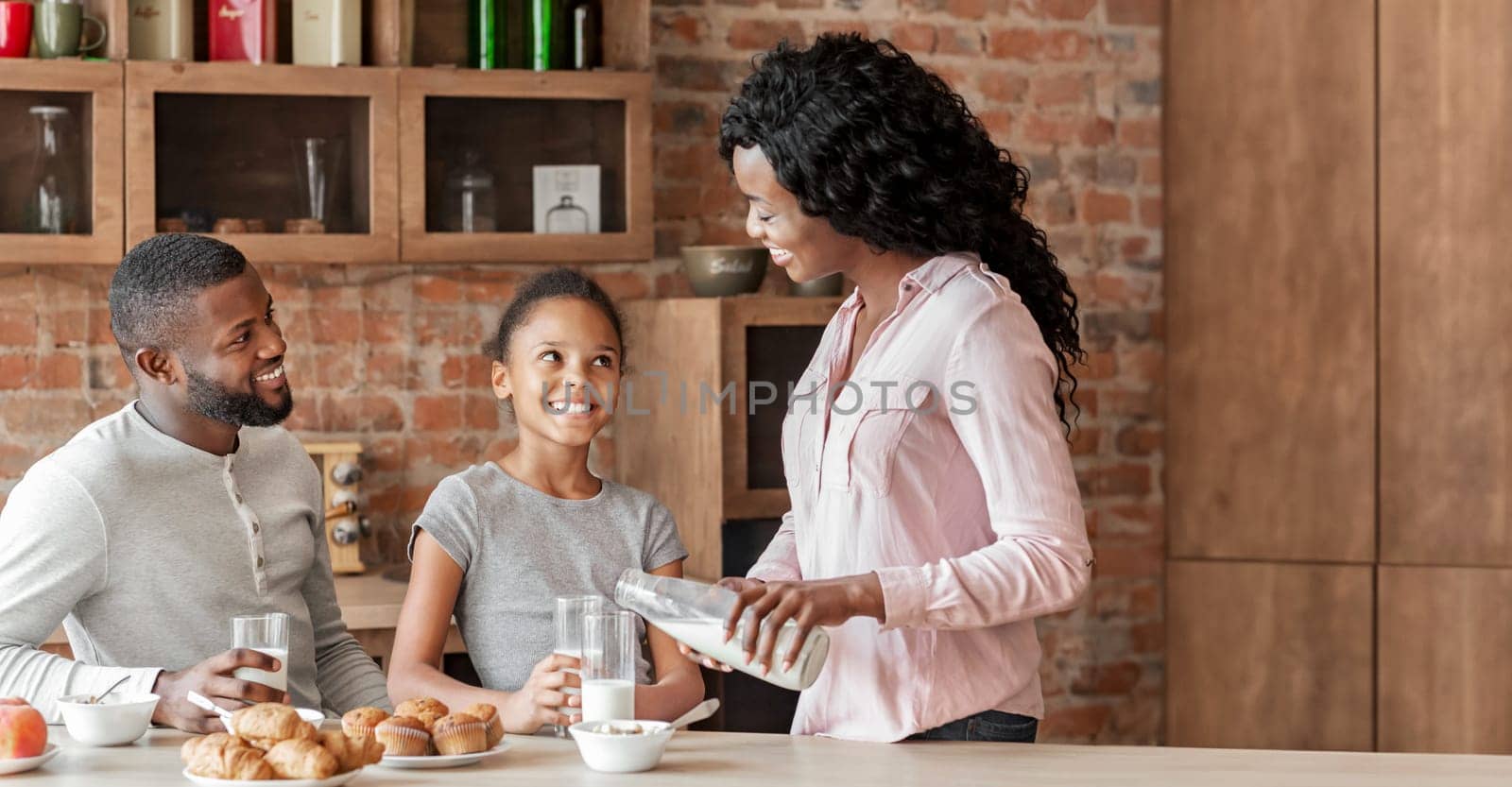 Little afro girl having breakfast with parents in kitchen, happy together, copy space