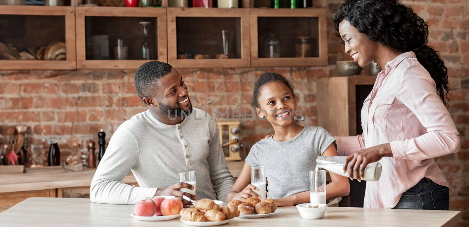 Calcium daily dose. Beautiful black woman pouring milk for her family, copy space